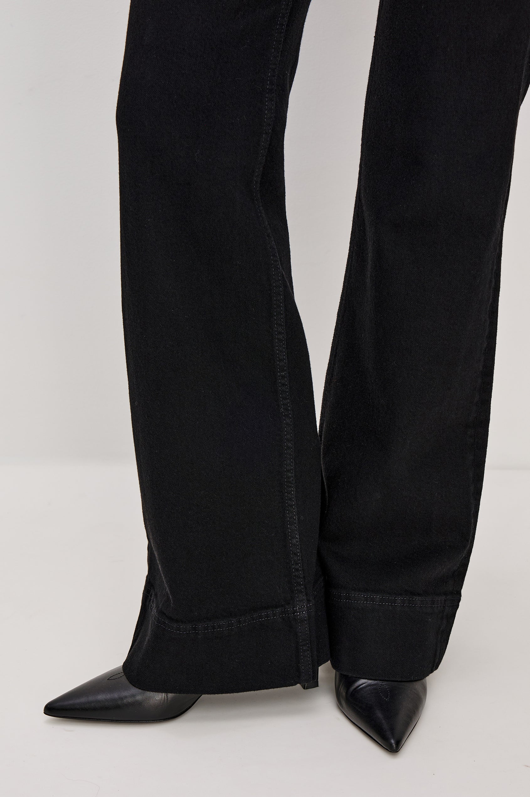 Alamitos is a high waisted denim trouser with flared leg and front patch pockets in Blackout colorway. Detail hem view featured on model.