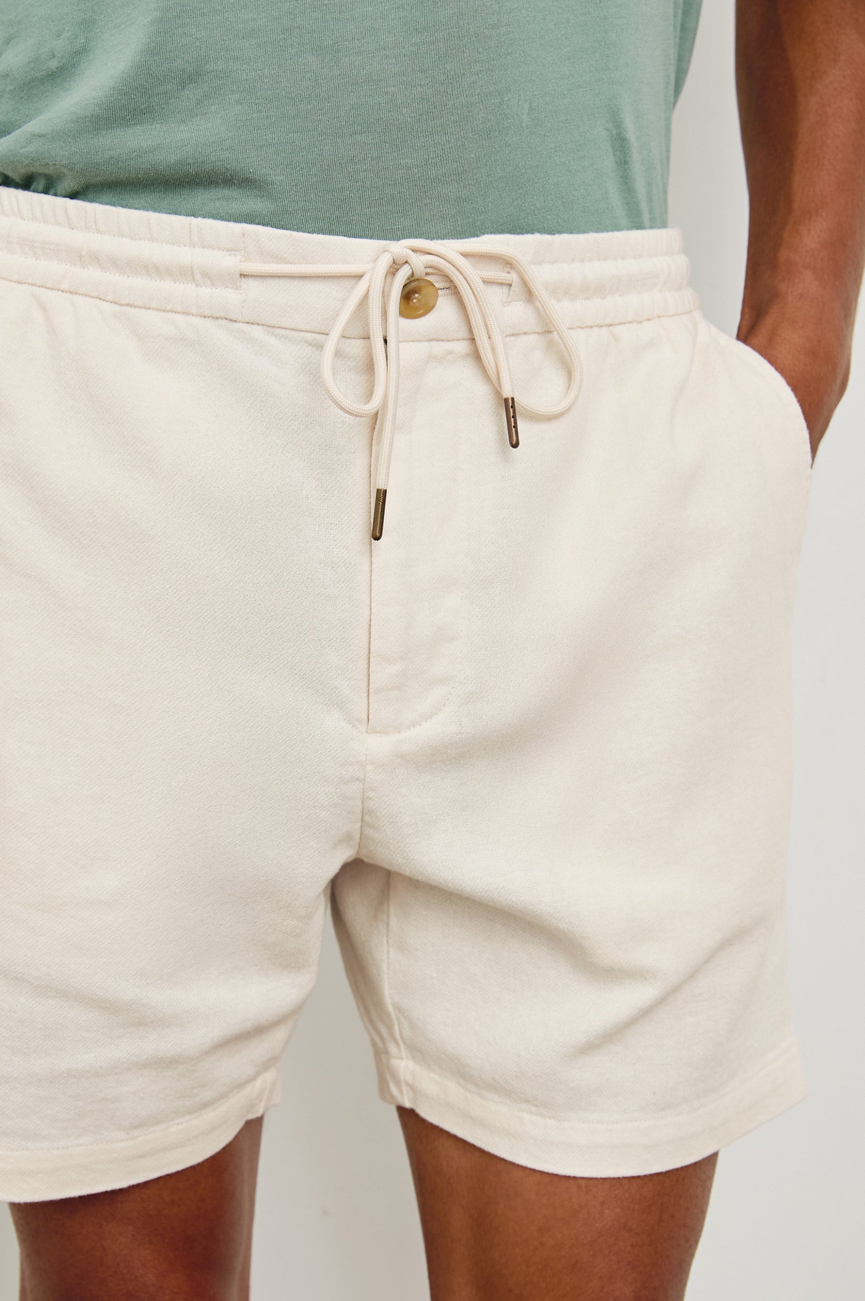 Archer medium length cotton short with adjustable drawstring and front button closure in Ecru - front view on model, hand in pocket