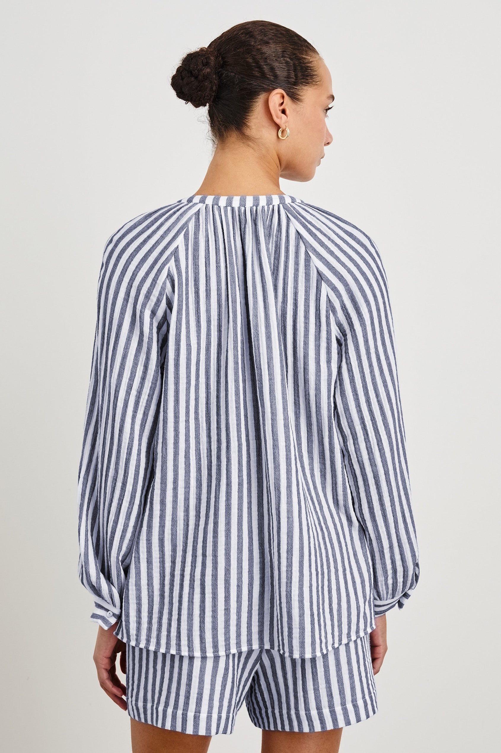 Back view of model wearing our Brielle Top, an airy style with a mandarin collar, raglan sleeves and front ties. Print is a blue and white vertical stripe. Styled with matching striped shorts.