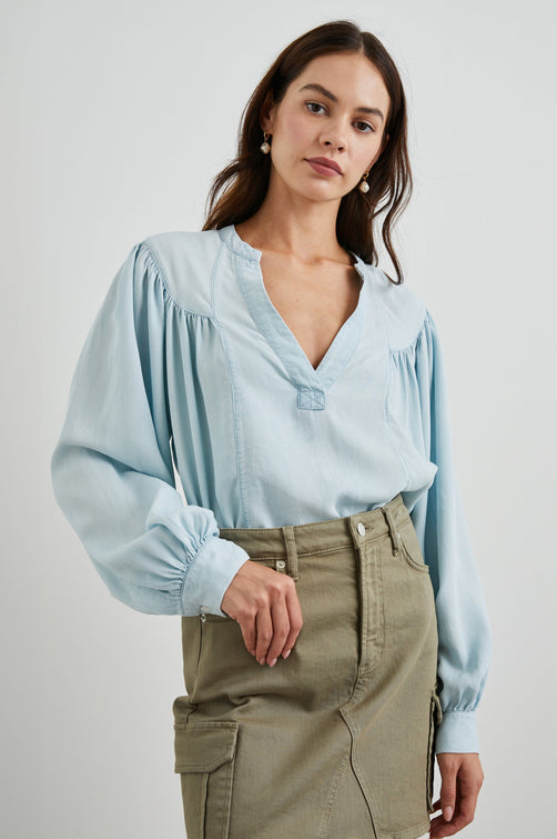 Fable Long Sleeve Top with a V Neck with a Placket, Buttoned Cuffs, and Pleating Down From the Yoke in Light Vintage Colorway, a Blue - Front Tucked View Featured on Model