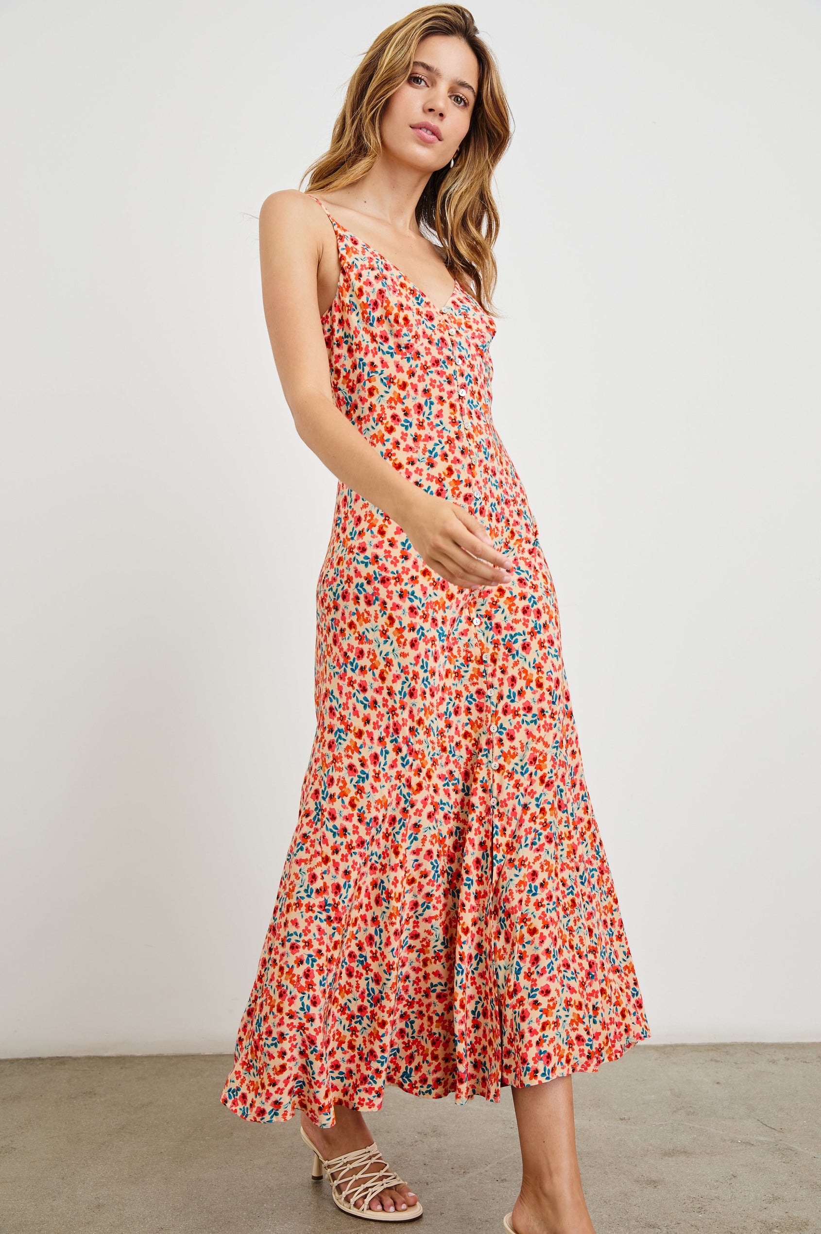 Florian Midi Dress with a V-Neckline, Spaghetti Straps, and Buttons down the front in Red Posy Colorway, Red, Blue and Orange on Tan - Side Full Body View Featured on model