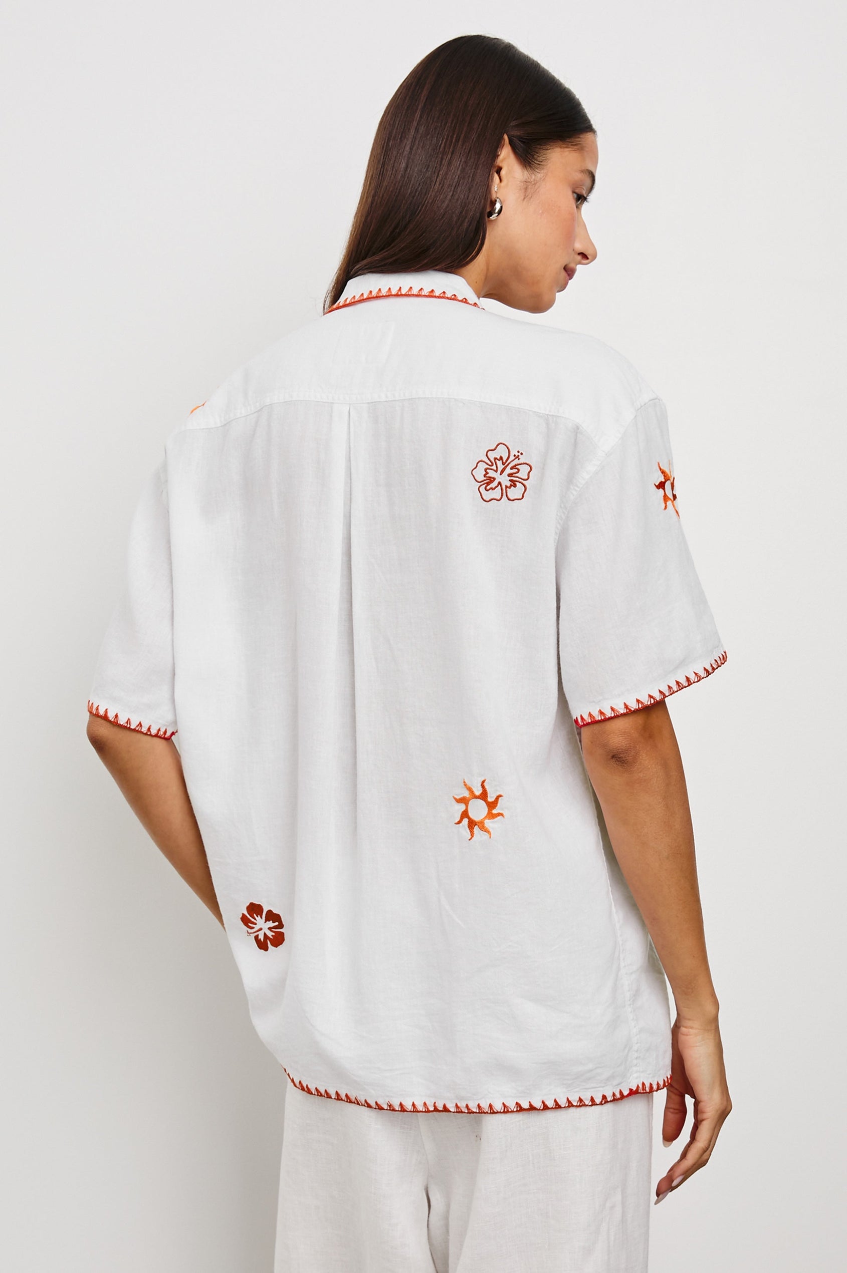 Island Short-Sleeve, Button-Down Shirt with Flat Collar, Large Chest Patch Pocket, Embroidered Decorative Trim and Embroidered Flowers and Sun in Red and Yellows in White Colorway - Back View Featured on Model