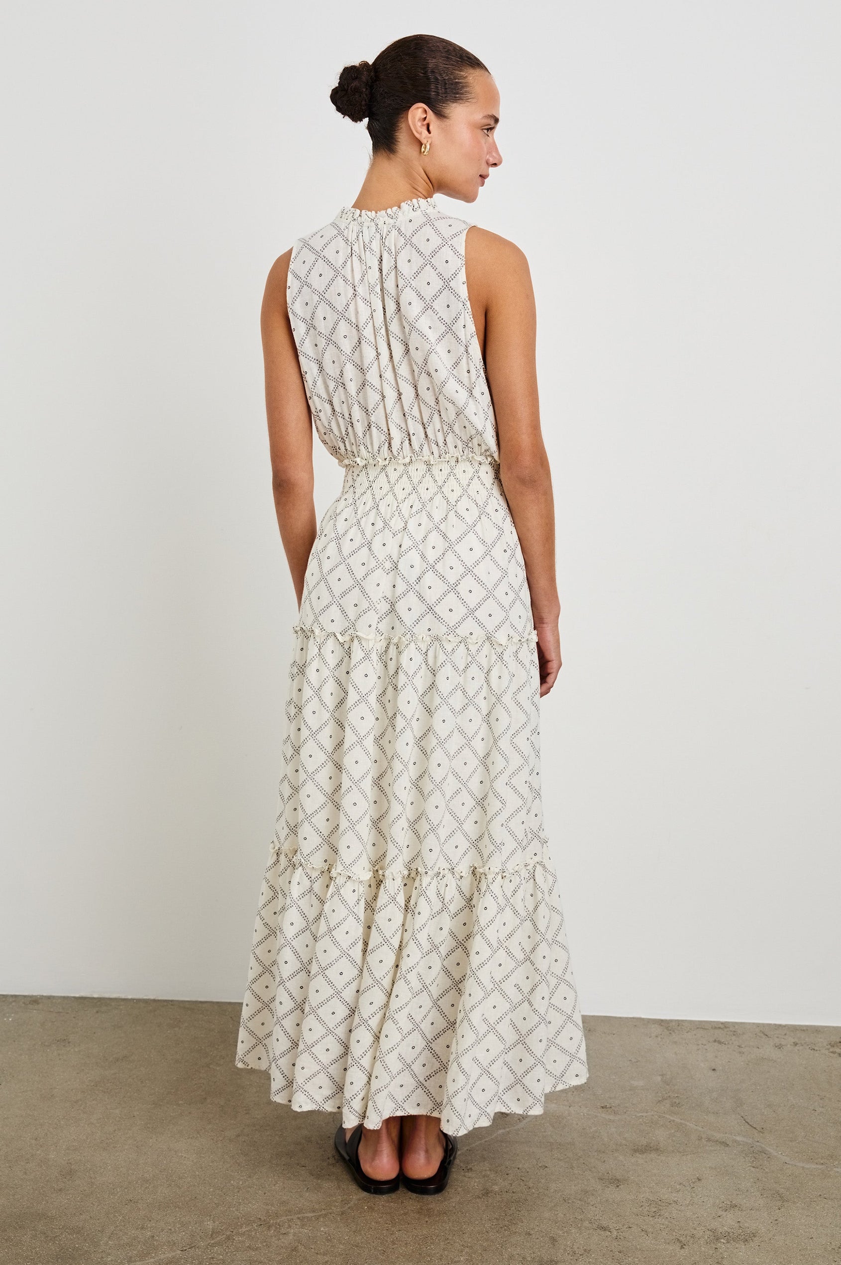 Back view of female model is wearing the Loulou Maxi Dress in a black and white boho print. Dress is Ivory with black printed details. Features smocking at the waist, a v-neckline and fully-lined skirt with ruffle detail at each tier.