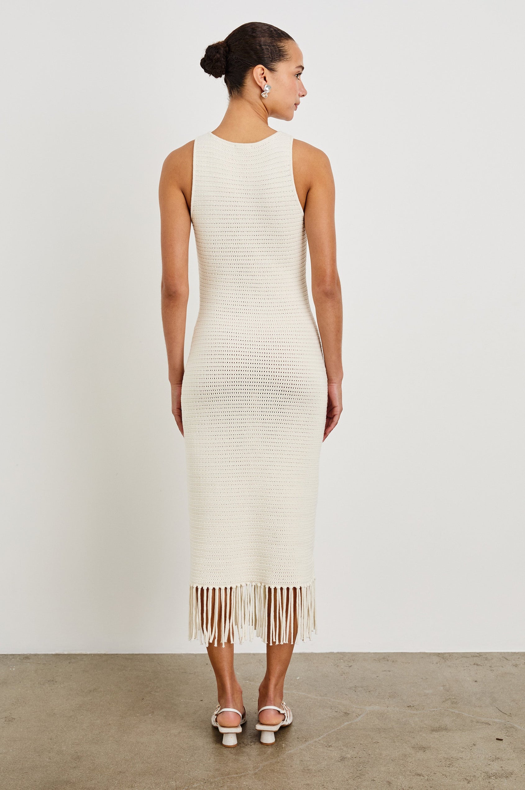 Back shot of female model wearing our sleeveless, Nia Midi Dress in color Ecru, featuring crochet structure and fringe details at the hem.