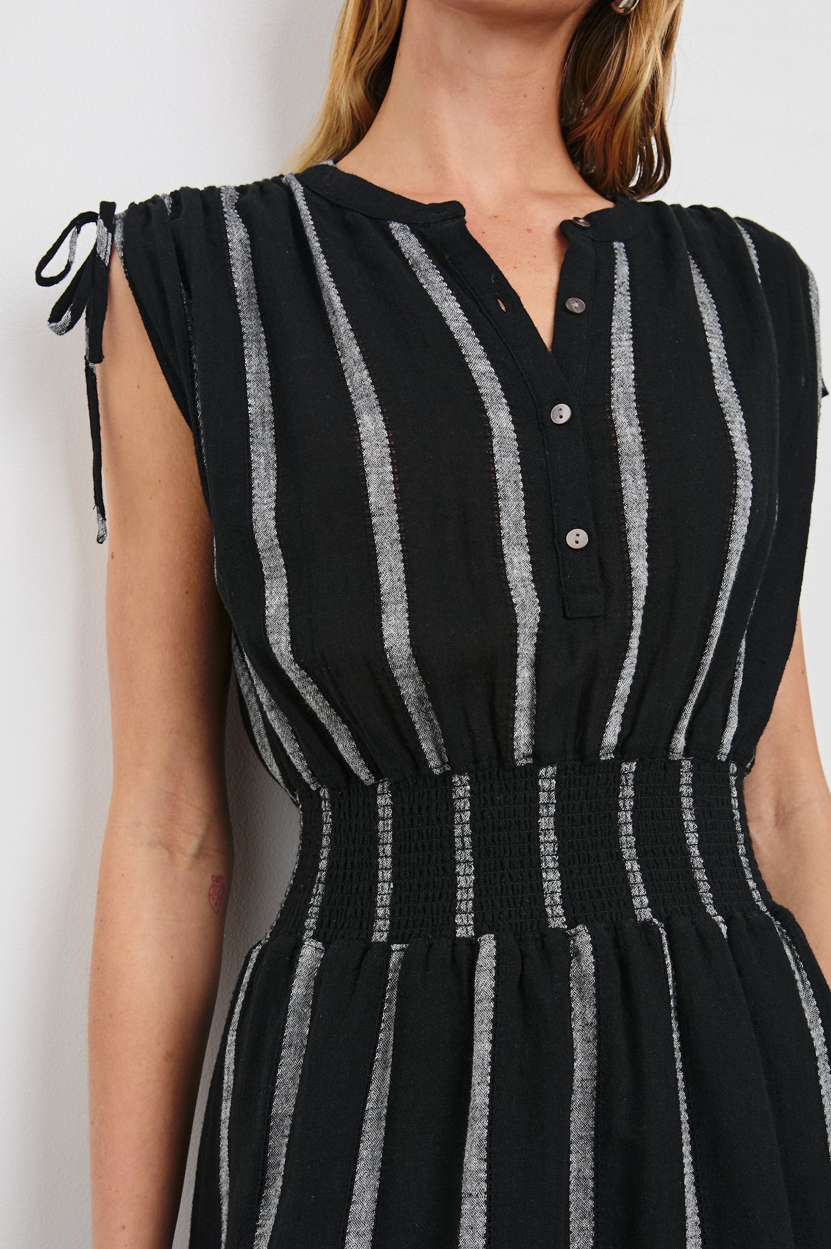 Samina Above-Knee Sleeveless Dress with drawstrings at the Arm Openings, Buttons along the Bodice, A Cinched Waist and a Tiered Skirt in Ash Leno Stripe Colorway, with Grey vertical stripes on black - Front View Featured on Model
