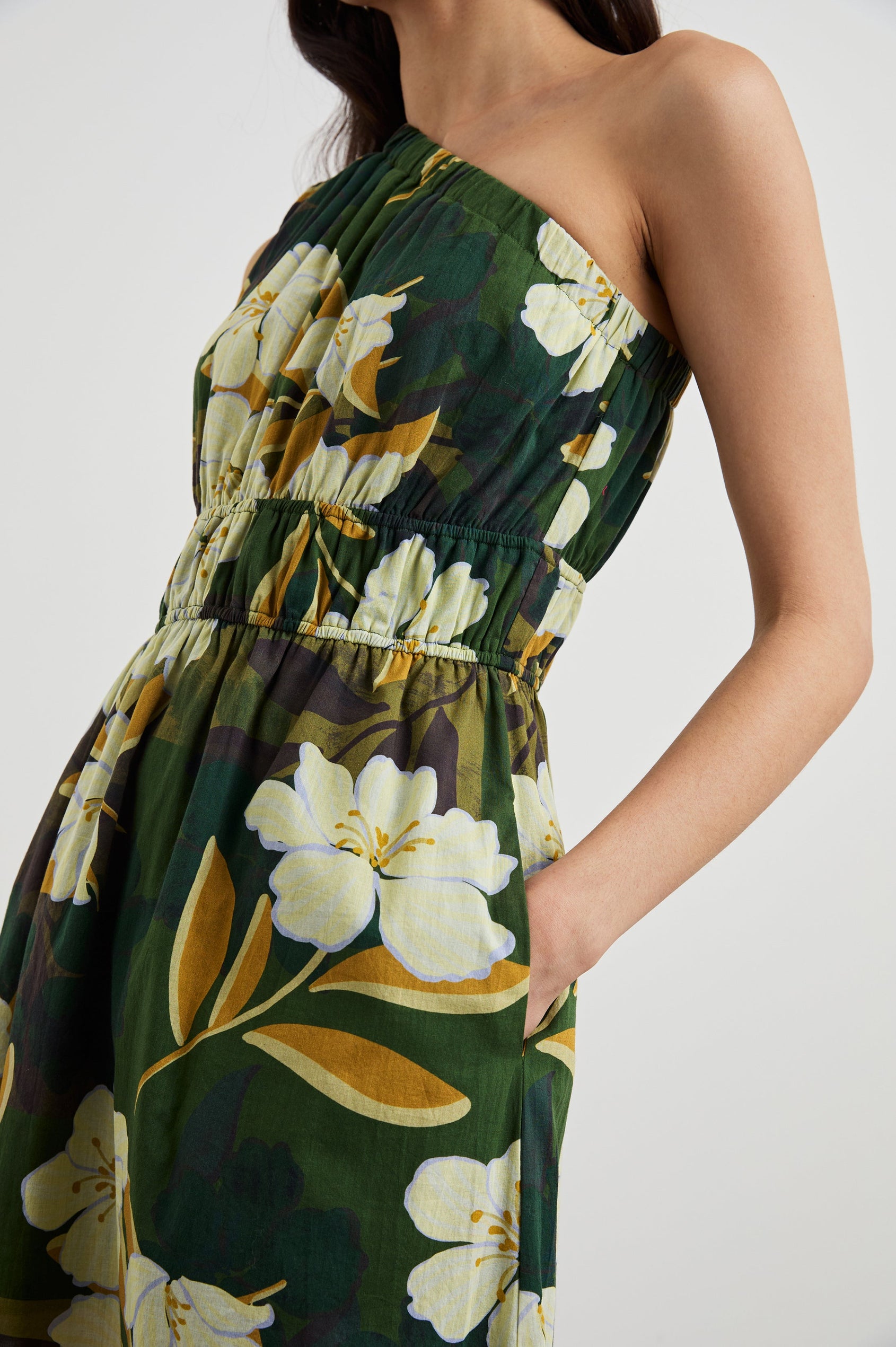 Selani Midi Dress With an Asymmetrical Neckline, Mid-Thigh Slide Slit and Cinched Waistband in Plumerias Colorway, with Ivory and Gold Plumerias on Dark Green - Side View Featured on Model