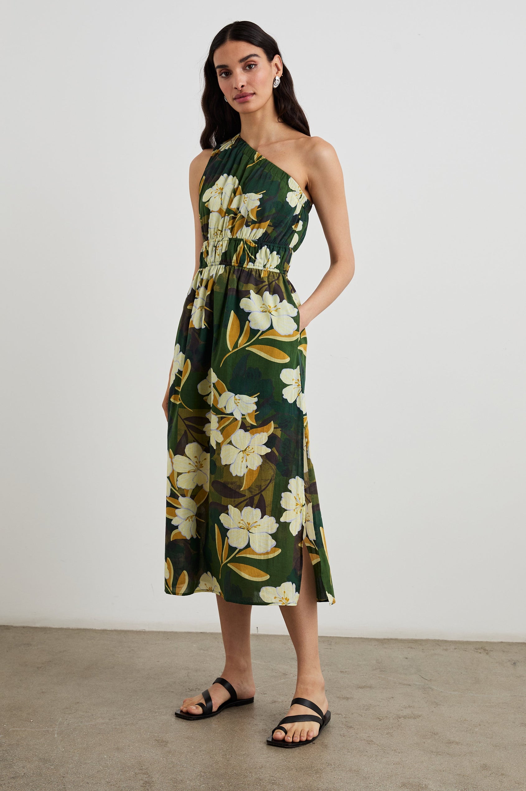 Selani Midi Dress With an Asymmetrical Neckline, Mid-Thigh Slide Slit and Cinched Waistband in Plumerias Colorway, with Ivory and Gold Plumerias on Dark Green - Front Full Body View Featured on Model