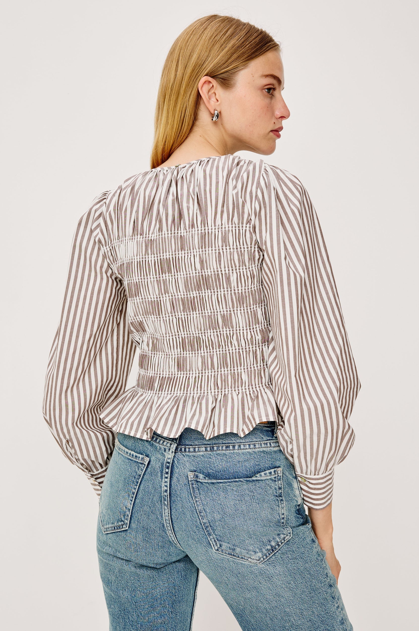 Tabi is a long sleeve crew neck top with puff sleeves and buttons at cuff, the bodice is pleated with a peplum hem in an Espresso Ivory Stripe colorway. Back view featured on model.