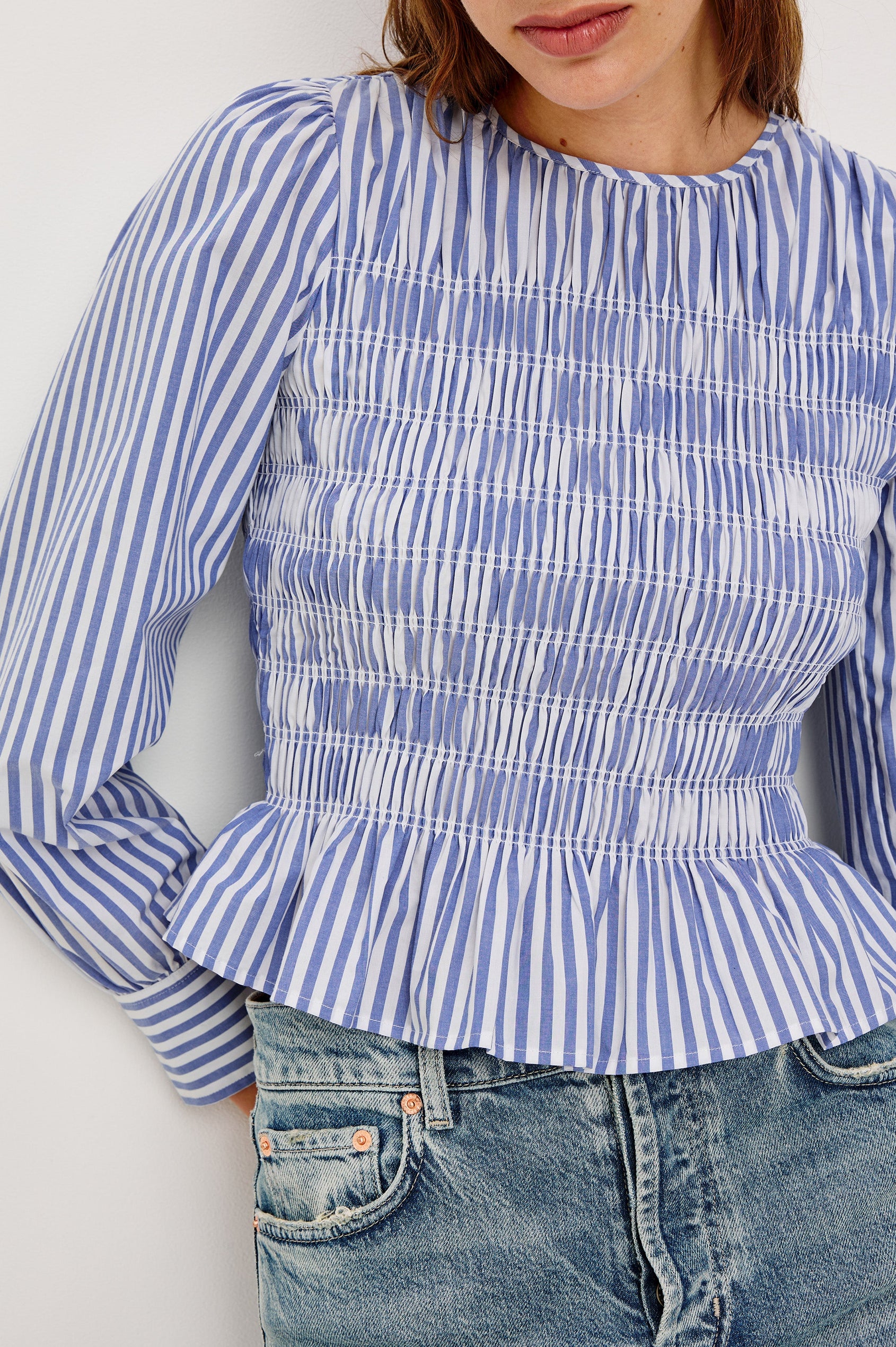 Tabi is a long sleeve crew neck top with puff sleeves and buttons at cuff, the bodice is pleated with a peplum hem in a blue Mariner White Stripe colorway. Front detail view featured on model.