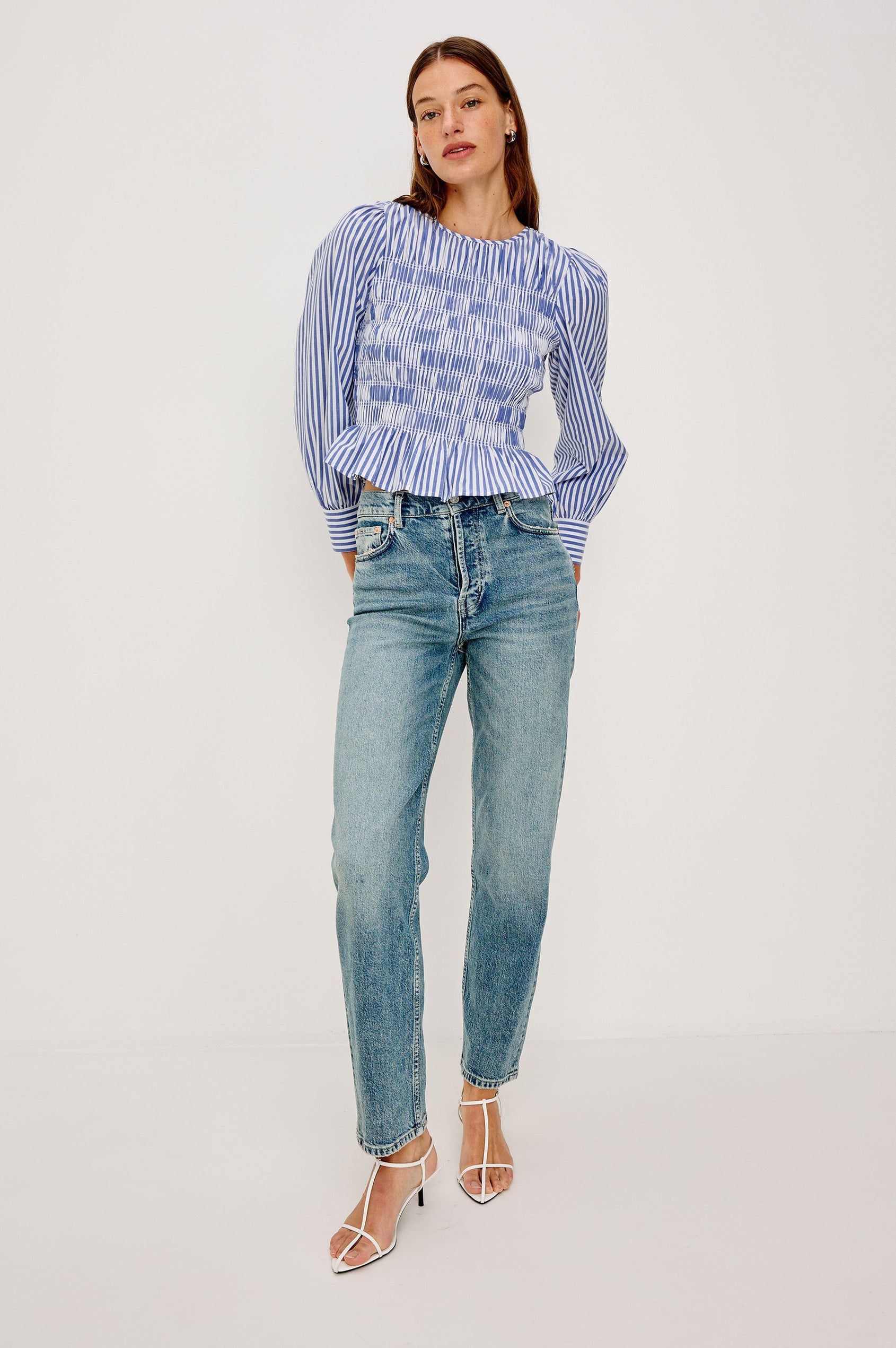 Tabi is a long sleeve crew neck top with puff sleeves and buttons at cuff, the bodice is pleated with a peplum hem in a blue Mariner White Stripe colorway. Front full body view featured on model.