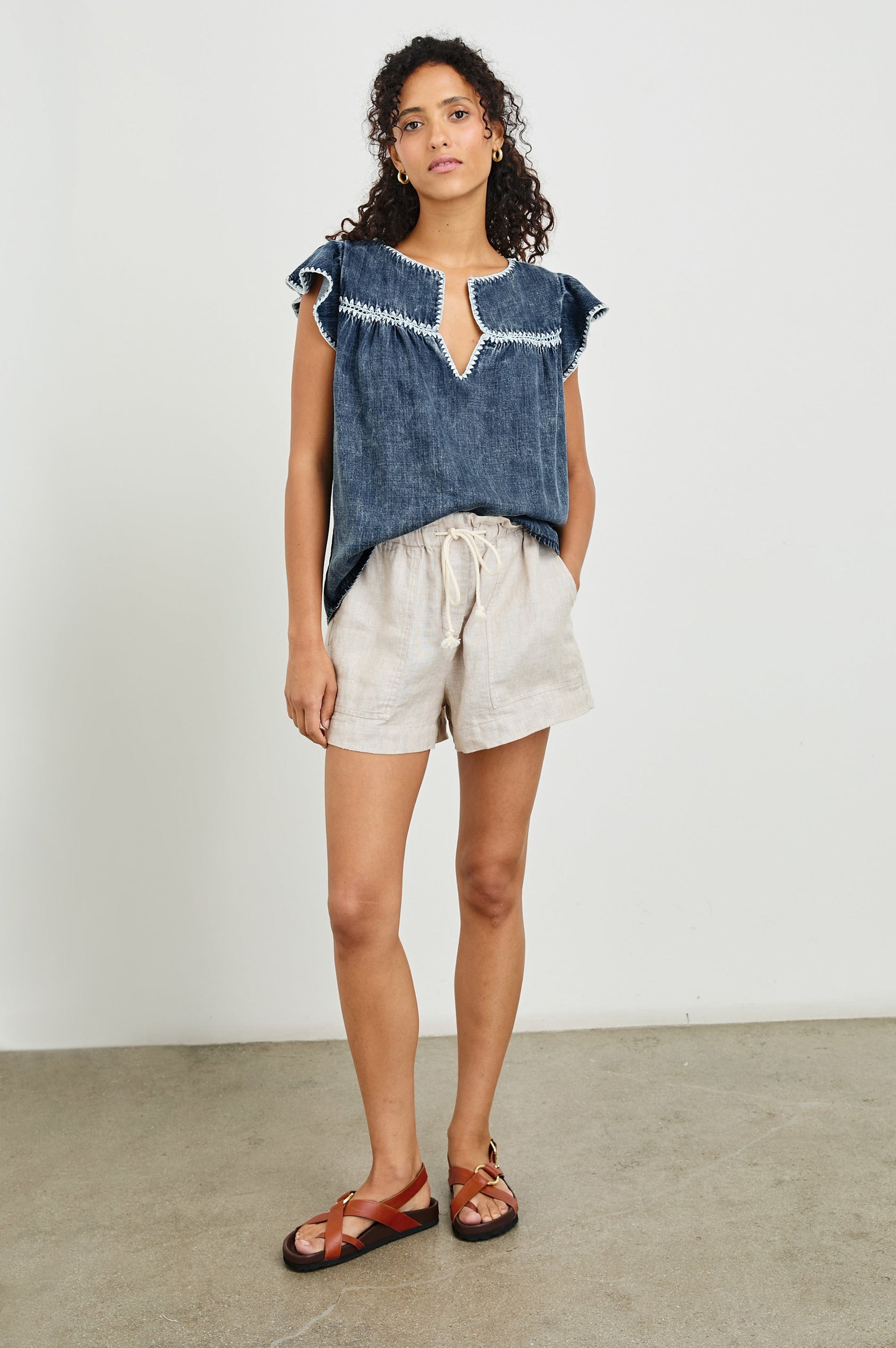 Tafia Top with an Open V-neck, Short Ruffle Cap Sleeves, and a White Blanket Stich along the Neckline, Cuffs and Yoke Seam in Classic Blue Colorway - Front Half-Tucked Full Body View Featured on Model