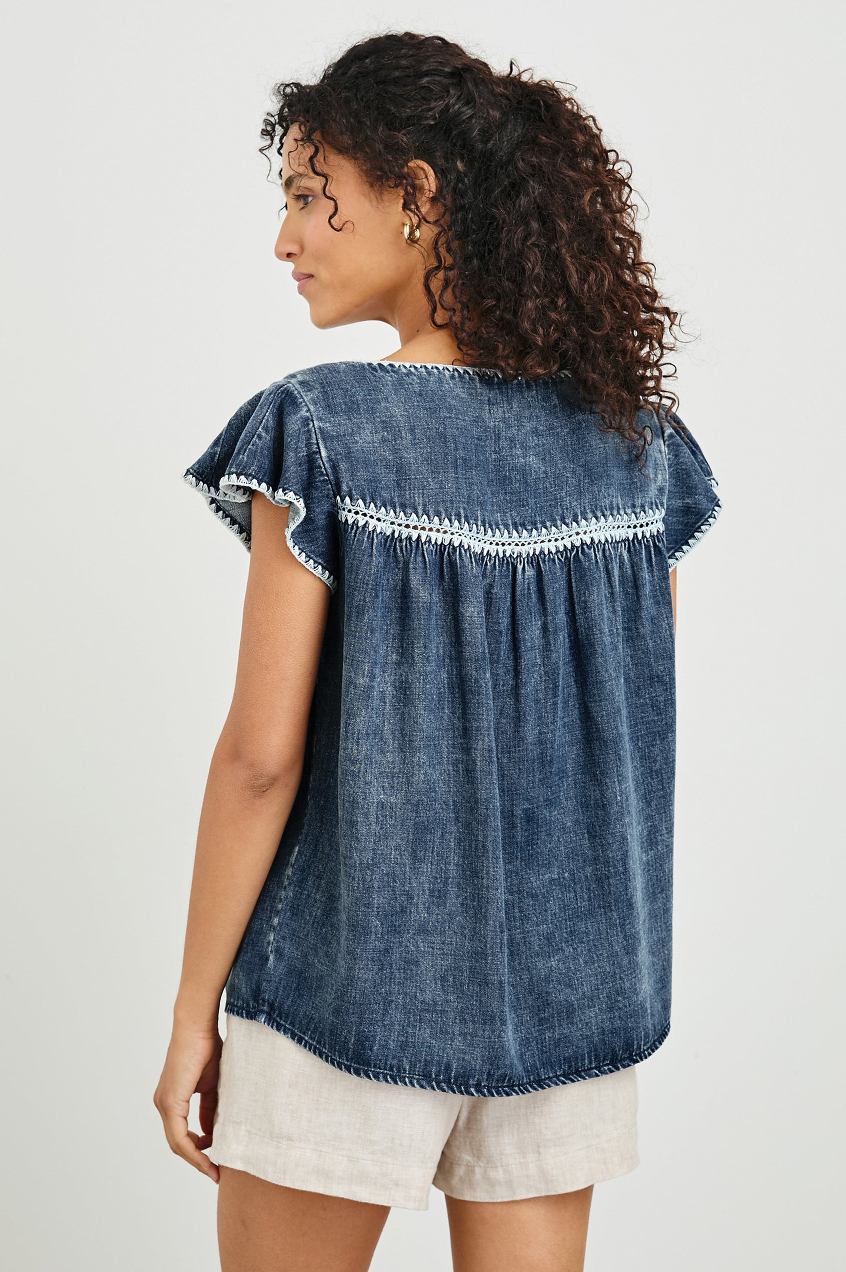 Tafia Top with an Open V-neck, Short Ruffle Cap Sleeves, and a White Blanket Stich along the Neckline, Cuffs and Yoke Seam in Classic Blue Colorway - Back Untucked View Featured on Model