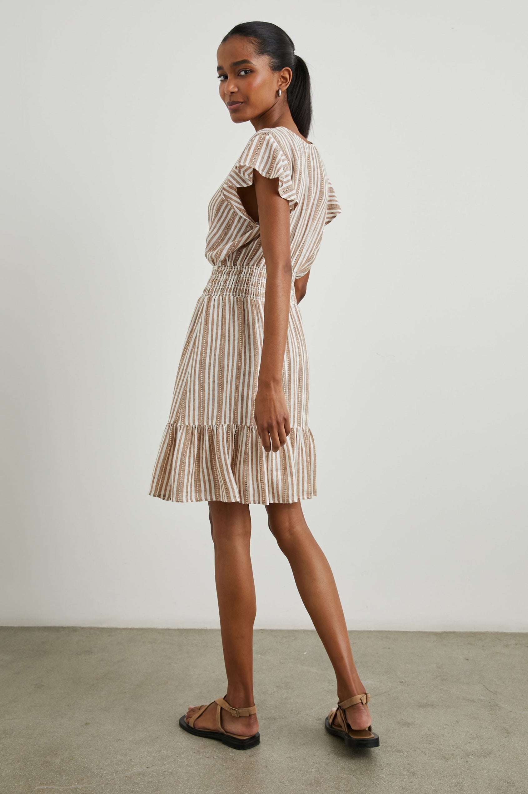 Tara Short Sleeve, Above the Knee Dress with a Smocked Waist, V Neck, Flutter Cap Sleeves, and Tiered Skirt with a Ruffled Hem in Palo Santo Stripe Colorway, with Textured Brown Vertical Stripes on White - Side Full Body View Featured on Model