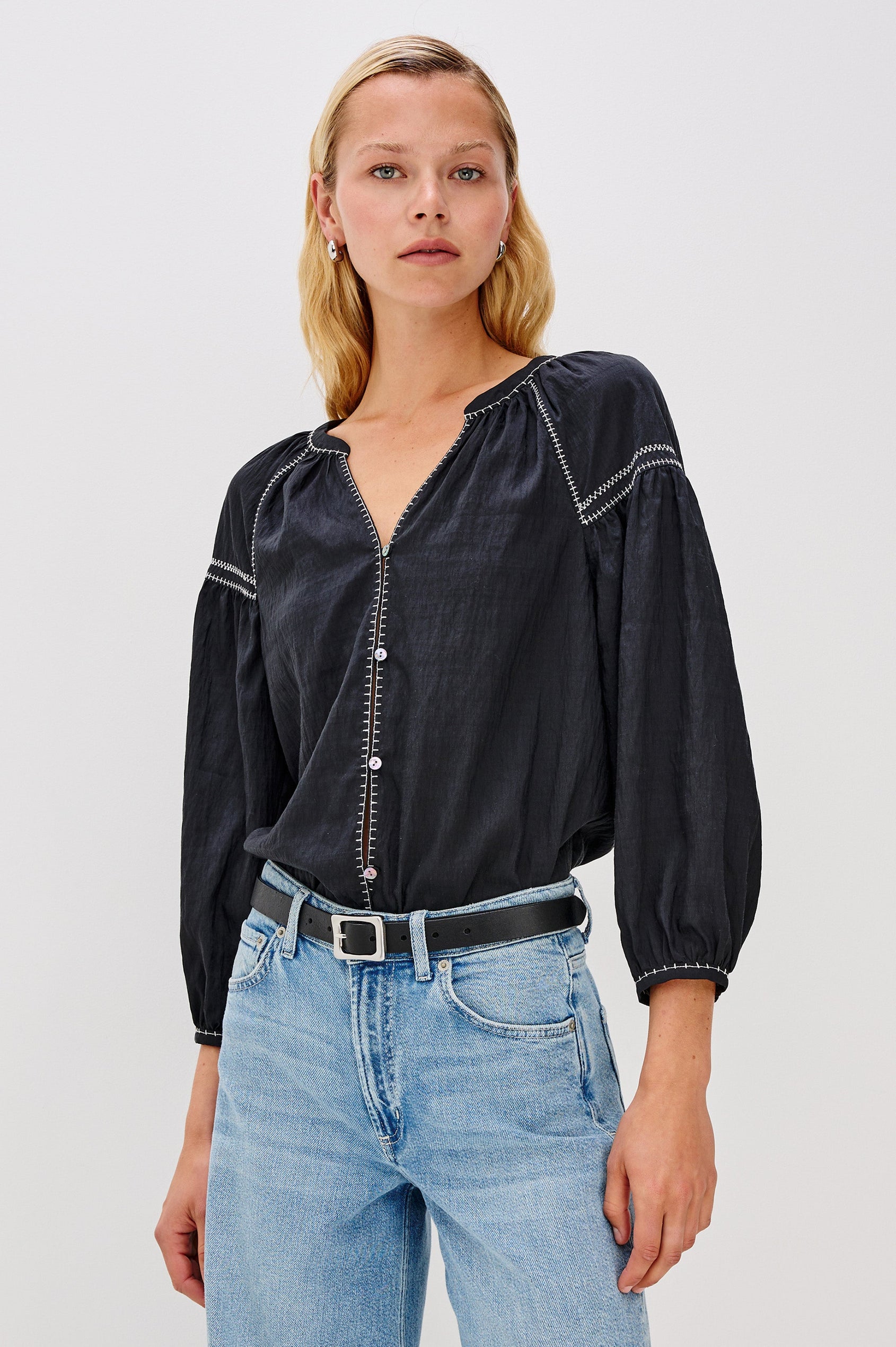 The Vasia is a long sleeve peasant top with a v-neck and button front, contrast white stitching and elastic at sleeve hems in Black colorway. Front view featured on model.