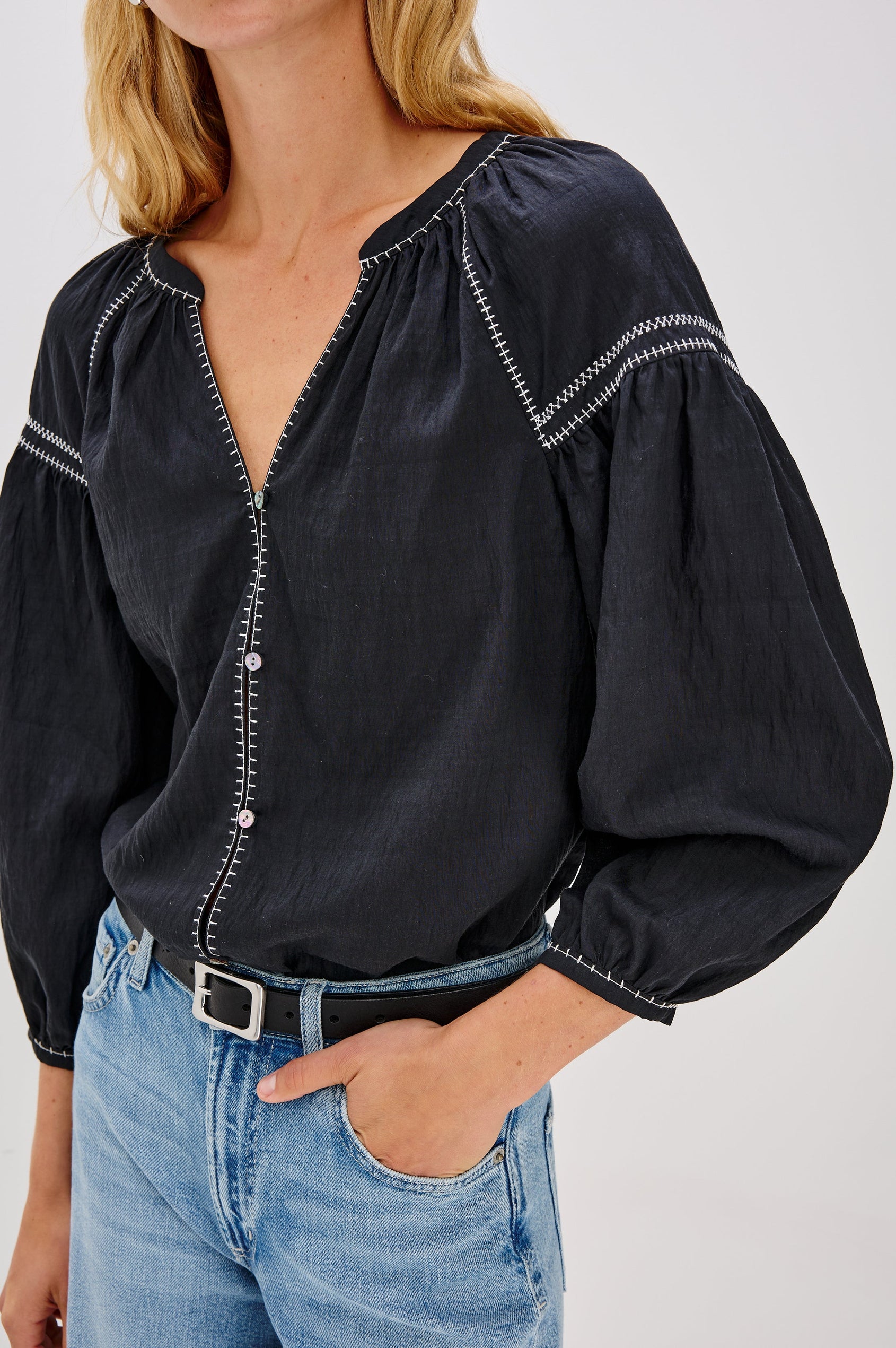 The Vasia is a long sleeve peasant top with a v-neck and button front, contrast white stitching and elastic at sleeve hems in Black colorway. Front detail view featured on model.