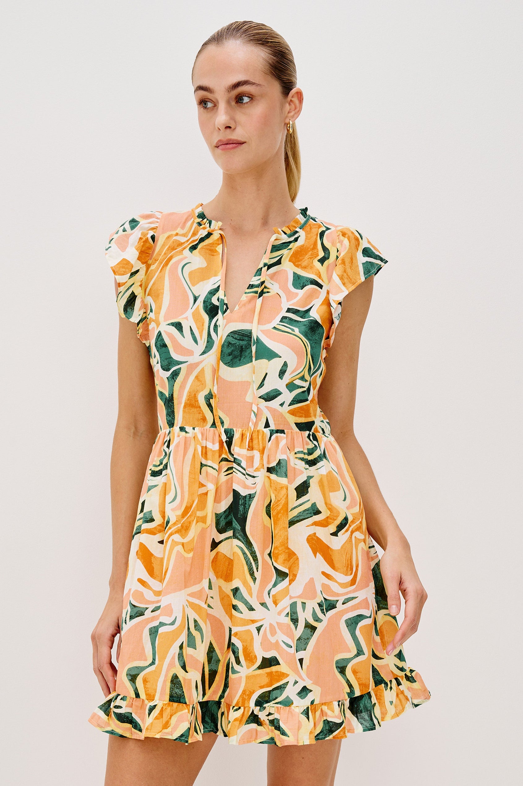 Zinnia Popover Mini Dress with Short Flutter Sleeves, Small Ruffle at Neck, V-Front with Self Tie Closure, Ruffle Hem in Tulum Colorway. Front View Shown on Model.