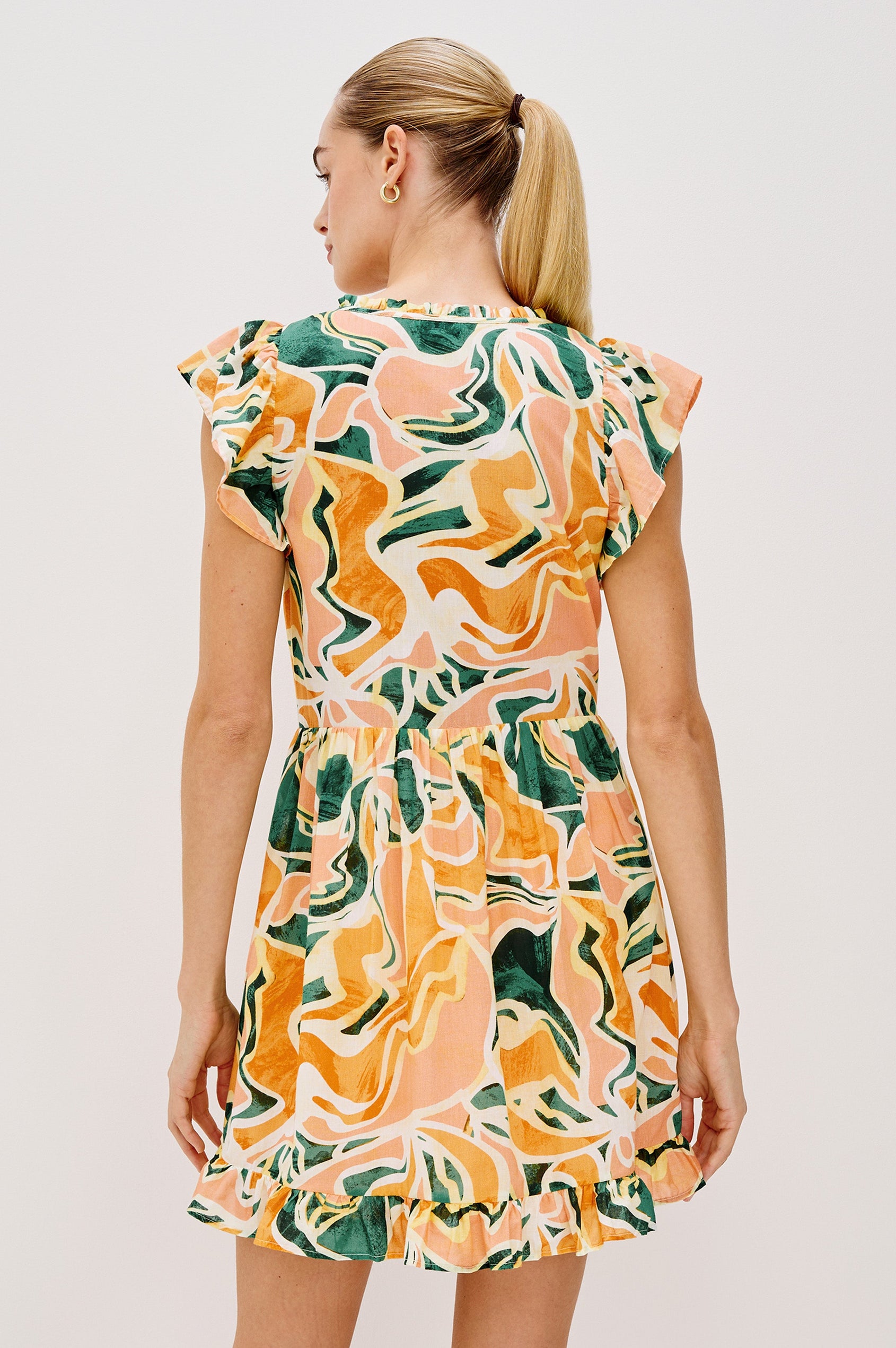 Zinnia Popover Mini Dress with Short Flutter Sleeves, Small Ruffle at Neck, V-Front with Self Tie Closure, Ruffle Hem in Tulum Colorway. Back View Shown on Model.