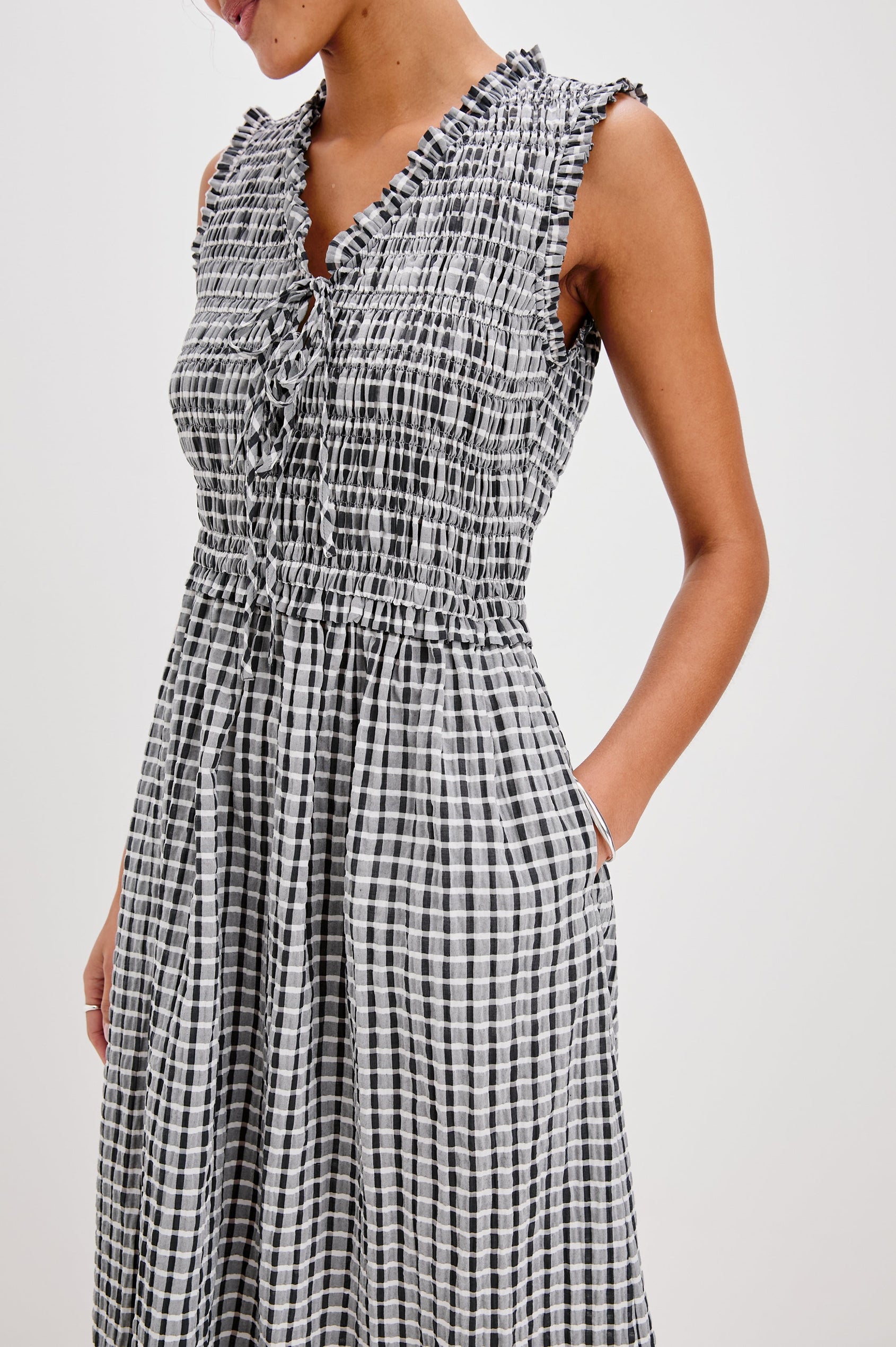 Adine Below-Knee Tank Dress with a Ruffle Edge V-Neck and Armhole, Tie Front, Gathered Bodice and A-Line Skirt in Ash Seersucker Colorway. Front Detailed View Shown on Model.