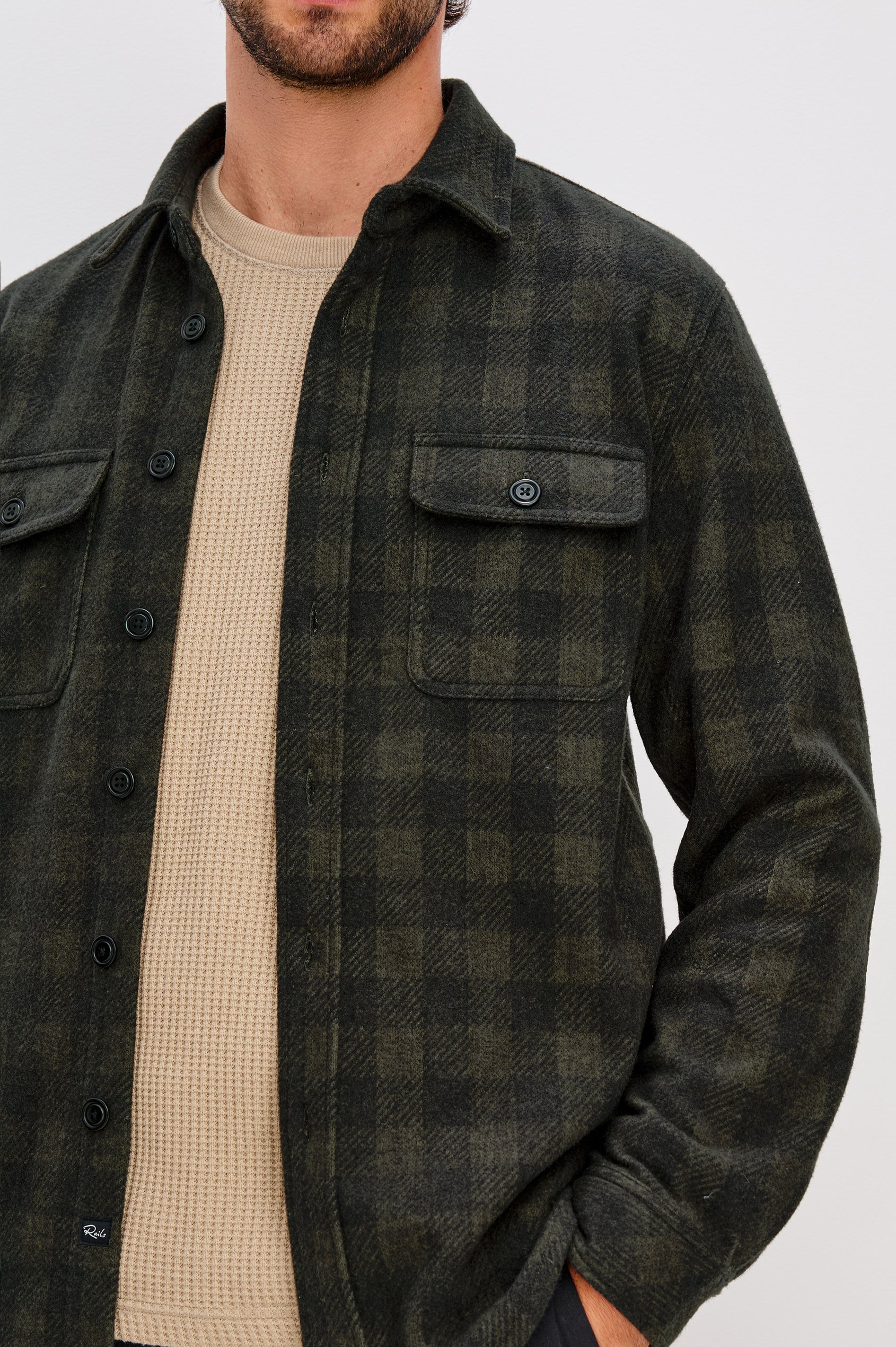 Alder Long-Sleeve Button up with Two Buttoned Chest Flap Pockets in Onyx Surplus Colorway, a Green and Black plaid. Front Unbuttoned Detail View Featured on Model