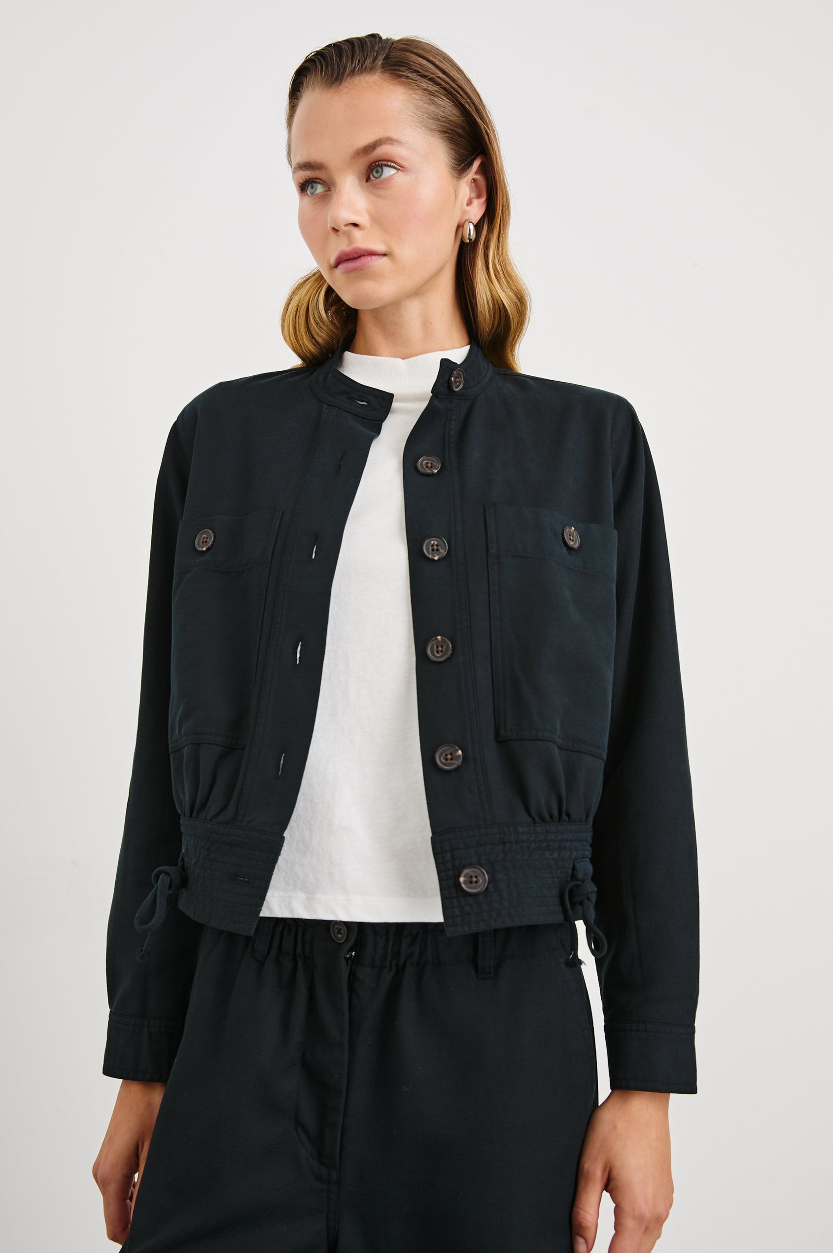 Alma Jacket with Button Closure, Mandarin Collar, Two Large Chest Button Patch Pockets and a Drawcord at the Hem in Black Colorway - Front View Featured on Model