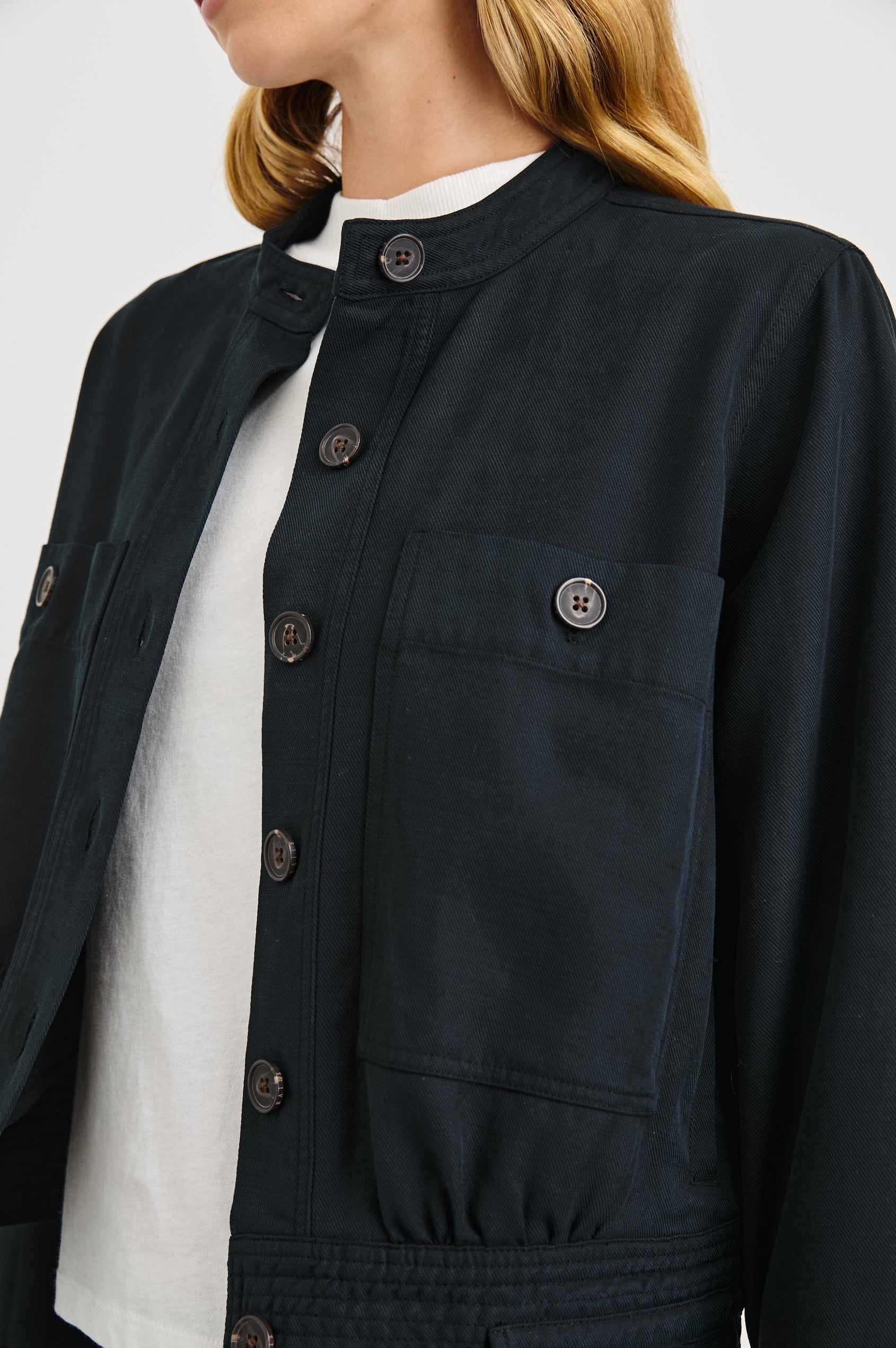 Alma Jacket with Button Closure, Mandarin Collar, Two Large Chest Button Patch Pockets and a Drawcord at the Hem in Black Colorway - Front View Featured on Model