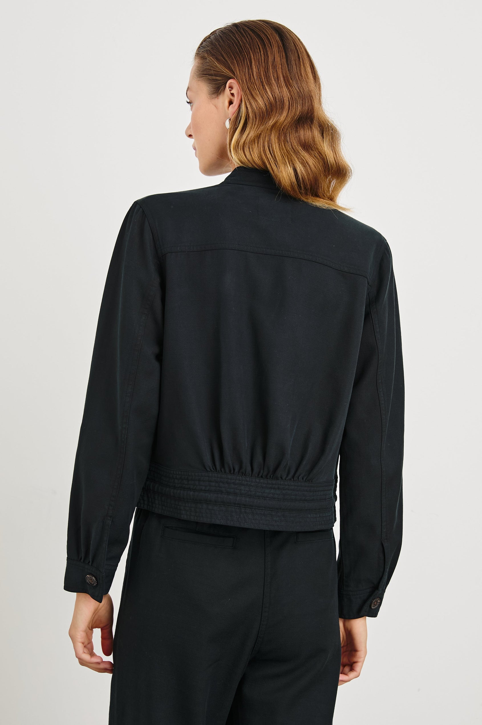 Alma Jacket with Button Closure, Mandarin Collar, Two Large Chest Button Patch Pockets and a Drawcord at the Hem in Black Colorway - Back View Featured on Model