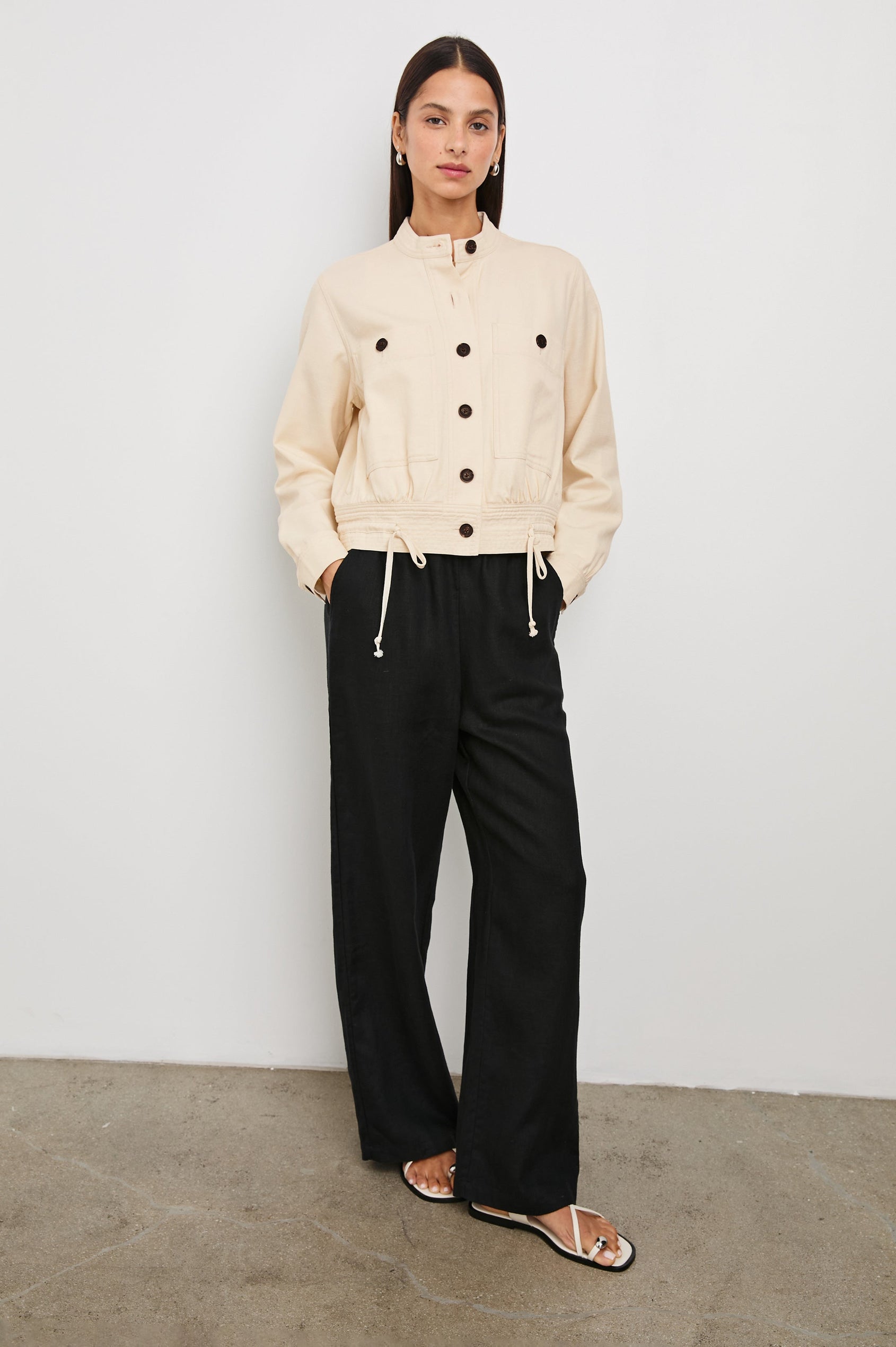 Alma Jacket with Button Closure, Mandarin Collar, Two Large Chest Button Patch Pockets and a Drawcord at the Hem in Ecru Colorway, with Dark Buttons - Front Full Body View Featured on Model