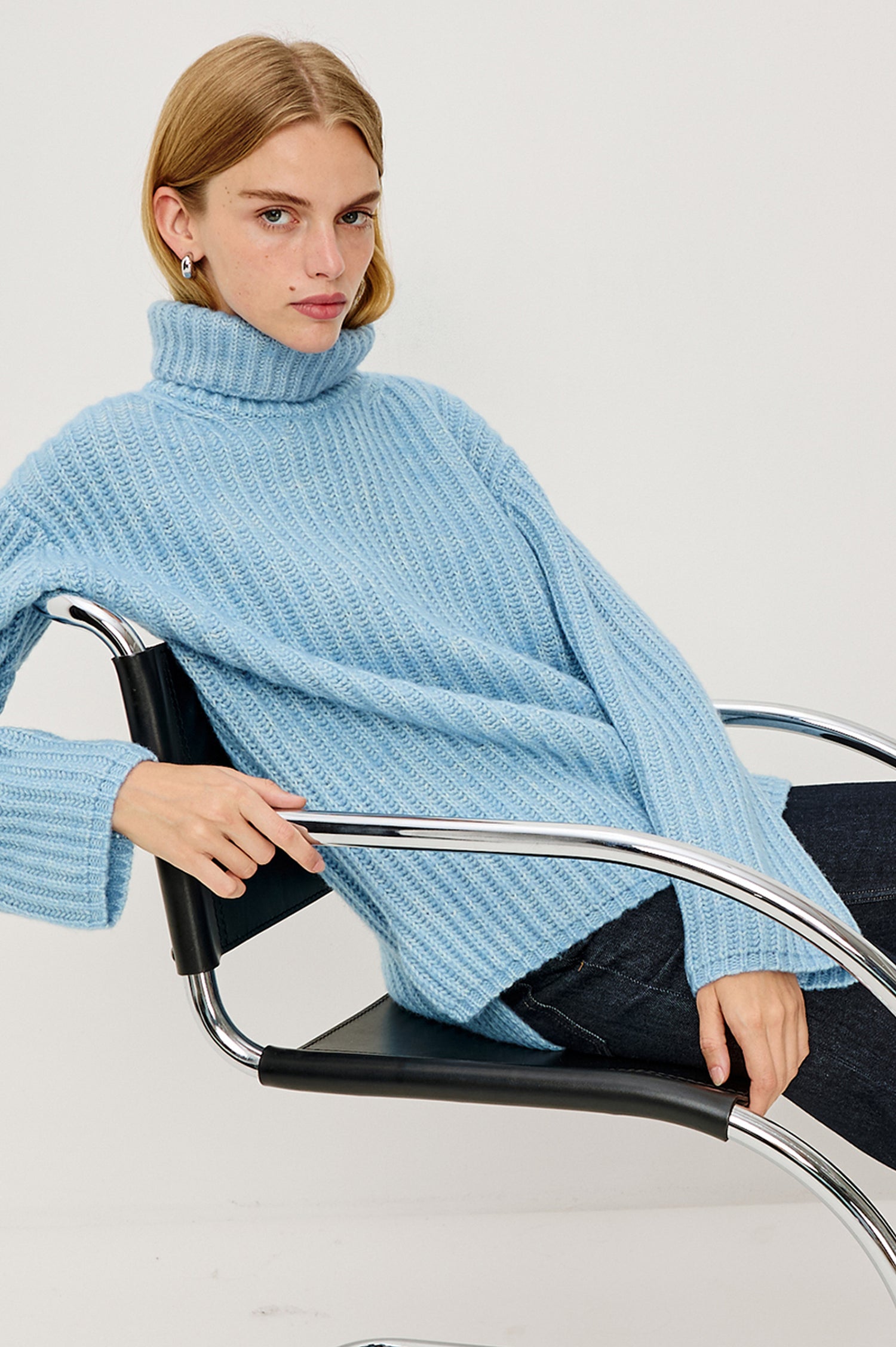 Anja Turtleneck Sweater in Soft Ribbed Knit With Relaxed Fit, High Low Hem, and Long Sleeves in Light Blue Colorway - Upper Body Side View Featured on Model Sitting