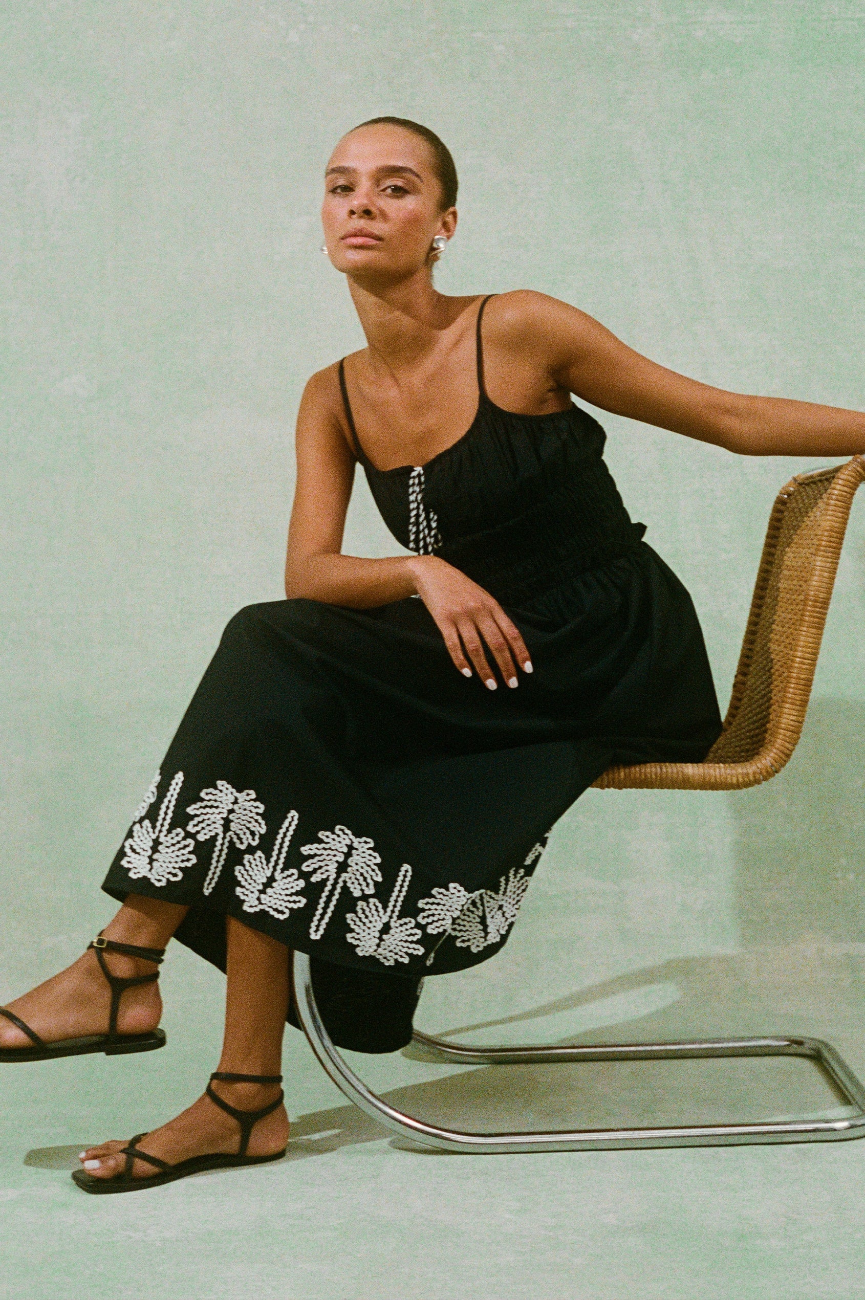 Baja Black Dress with Ivory Palm Tree Stitching at the skirt hem and neckline cord ties - model sitting on chair