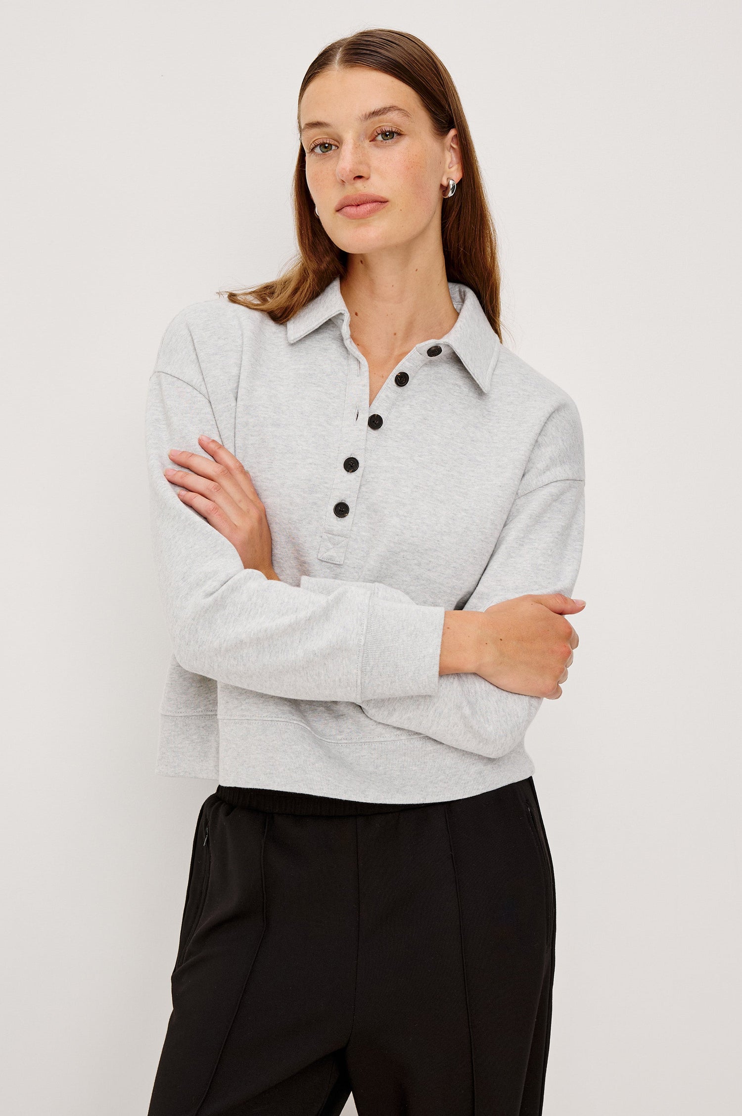 Cotton polo-style sweatshirt made from French terry fabric. The design features a button-front half placket, drop shoulders, and binding at the hem and cuffs for a relaxed, comfortable fit in Heather Grey Colorway - Front view featured on model with Arms Crossed