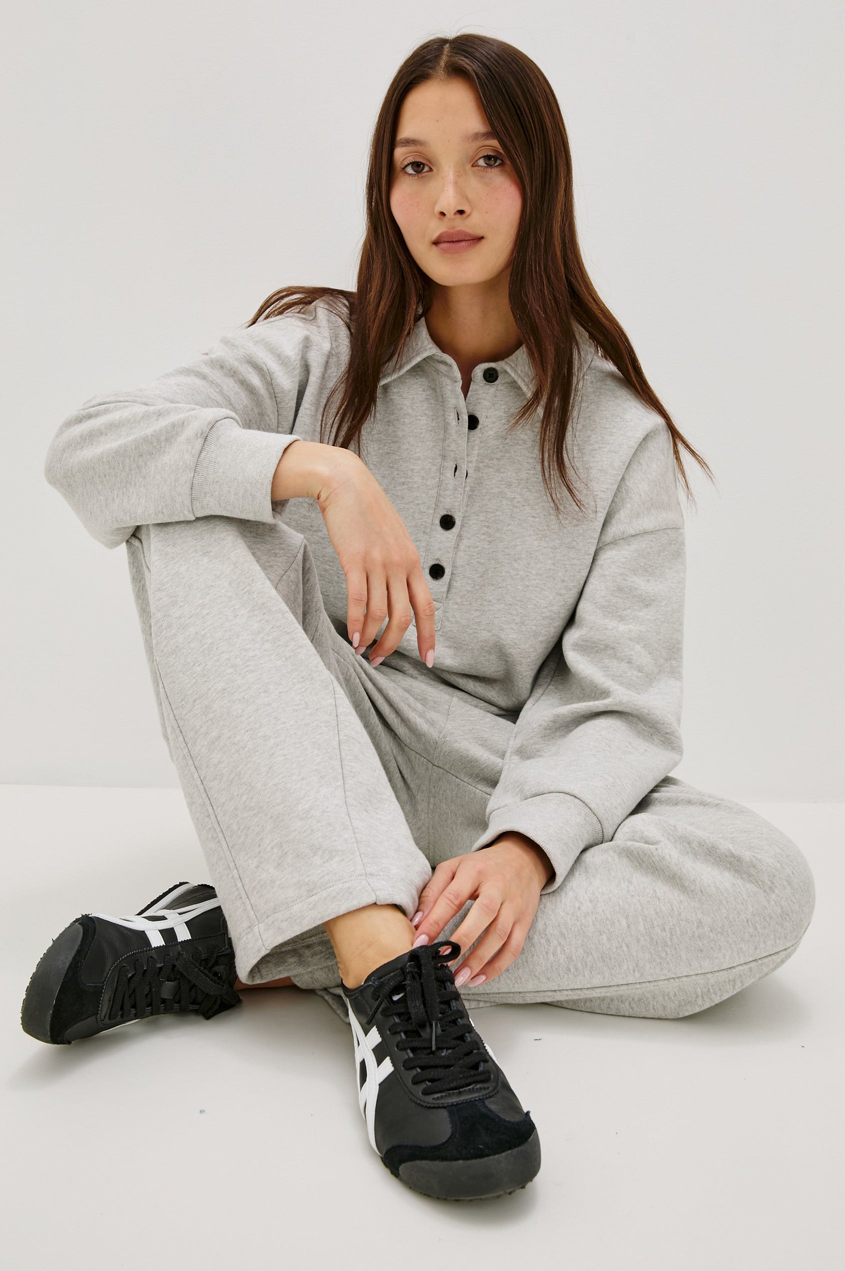 Cotton polo-style sweatshirt made from French terry fabric. The design features a button-front half placket, drop shoulders, and binding at the hem and cuffs for a relaxed, comfortable fit in Heather Grey Colorway - Front view featured on model, sitting with legs crossed