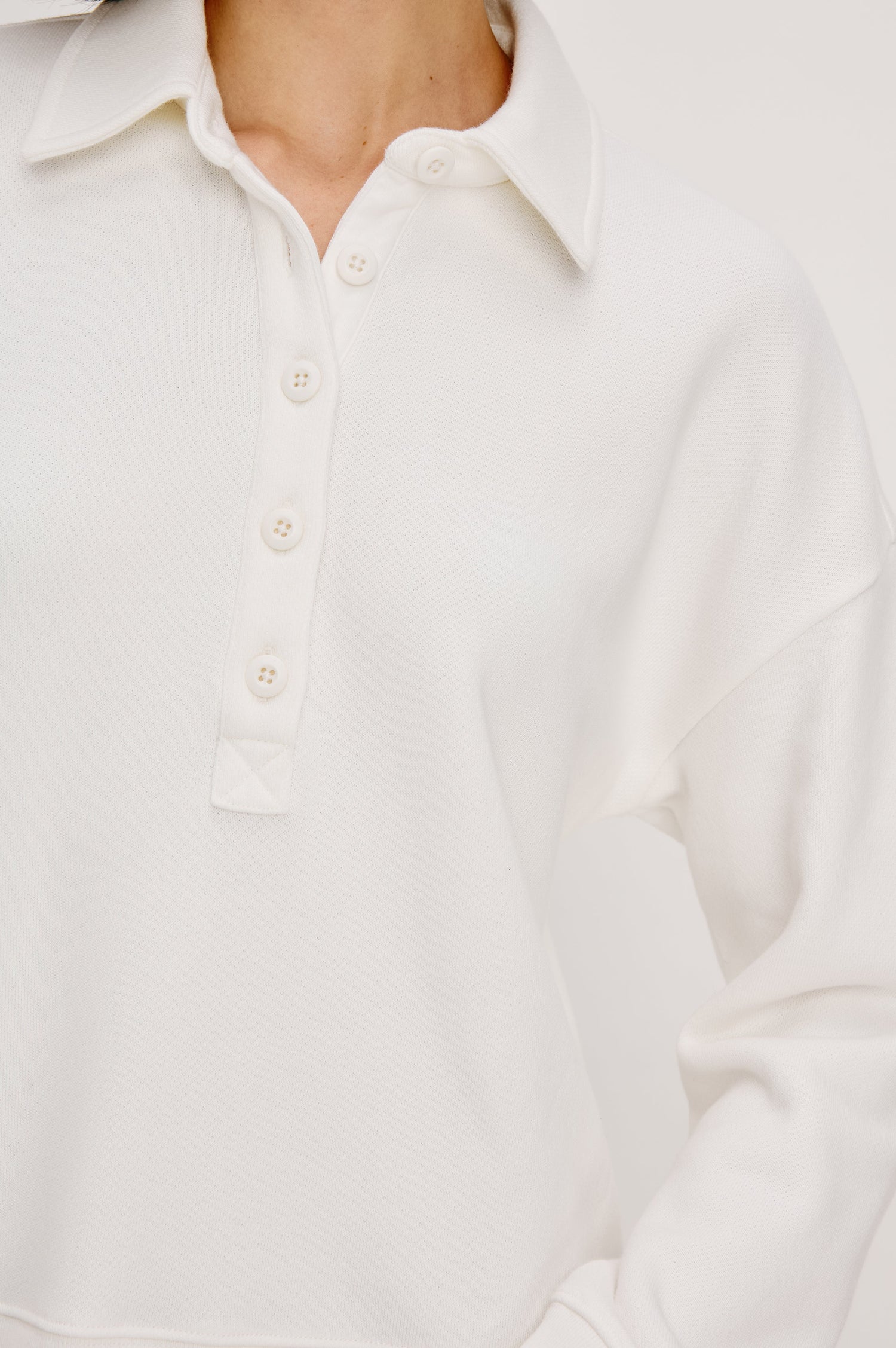 Cotton polo-style sweatshirt made from French terry fabric. The design features a button-front half placket, drop shoulders, and binding at the hem and cuffs for a relaxed, comfortable fit in Ivory Colorway - Close up of details featured on model