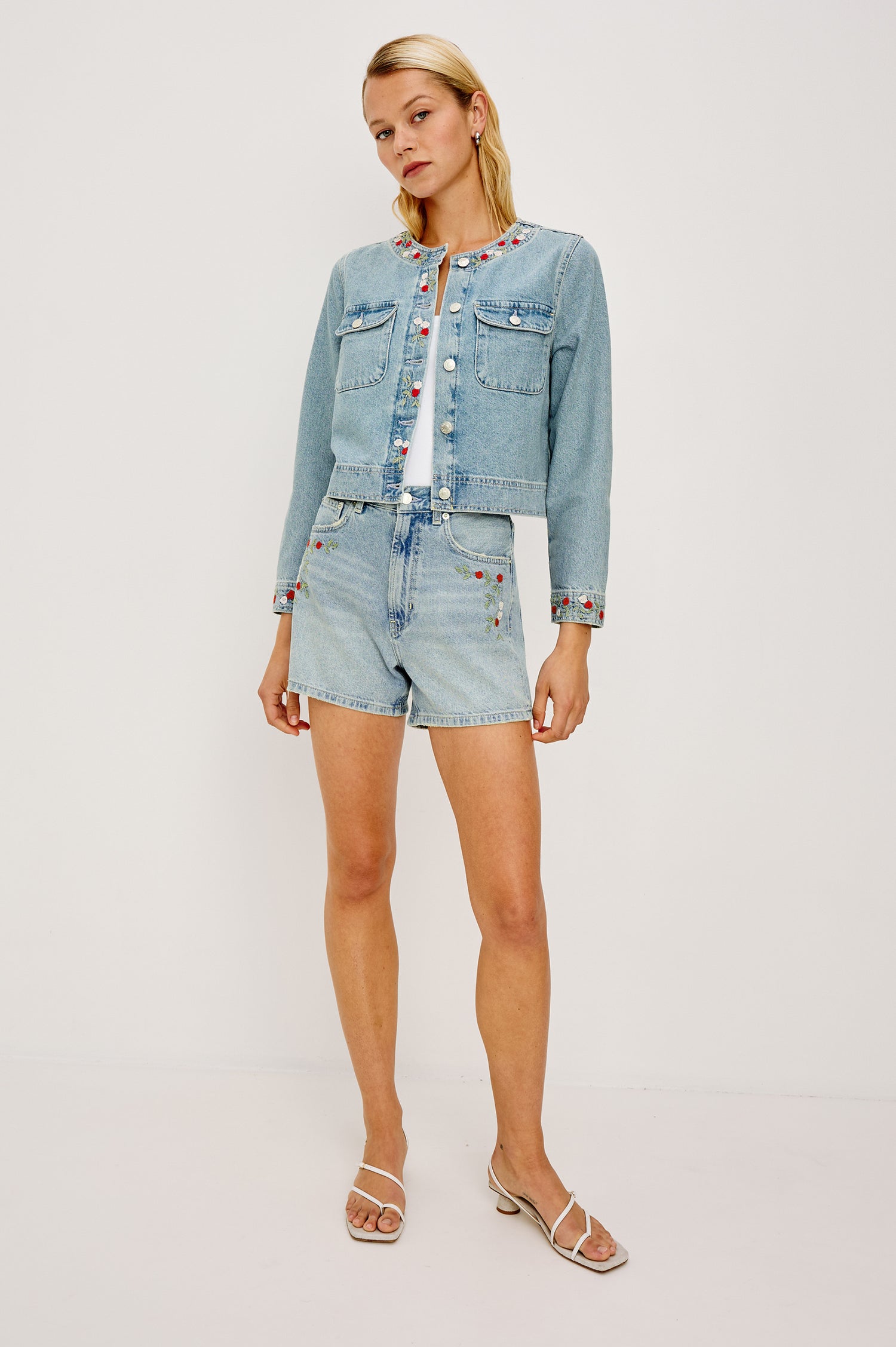 The Capistrano is a cropped denim jacket with a scoop neck, a button front, two chest pockets in Floral laser colorway. Full body front view featured on model.