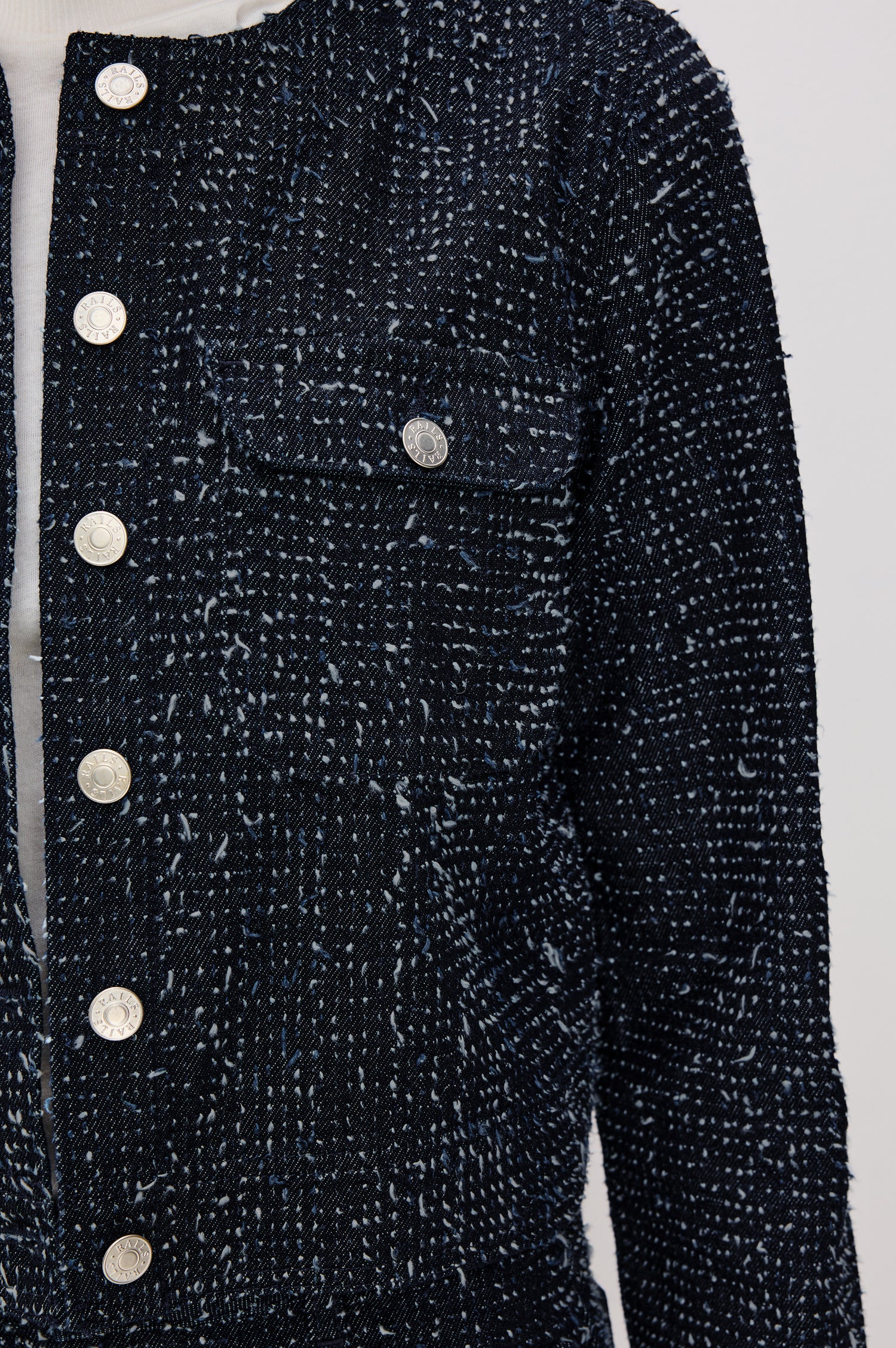 The Capistrano is a cropped denim jacket with a crewneck, it has a button front and two chest pockets in Denim Tweed colorway. Front detail view featured on model.
