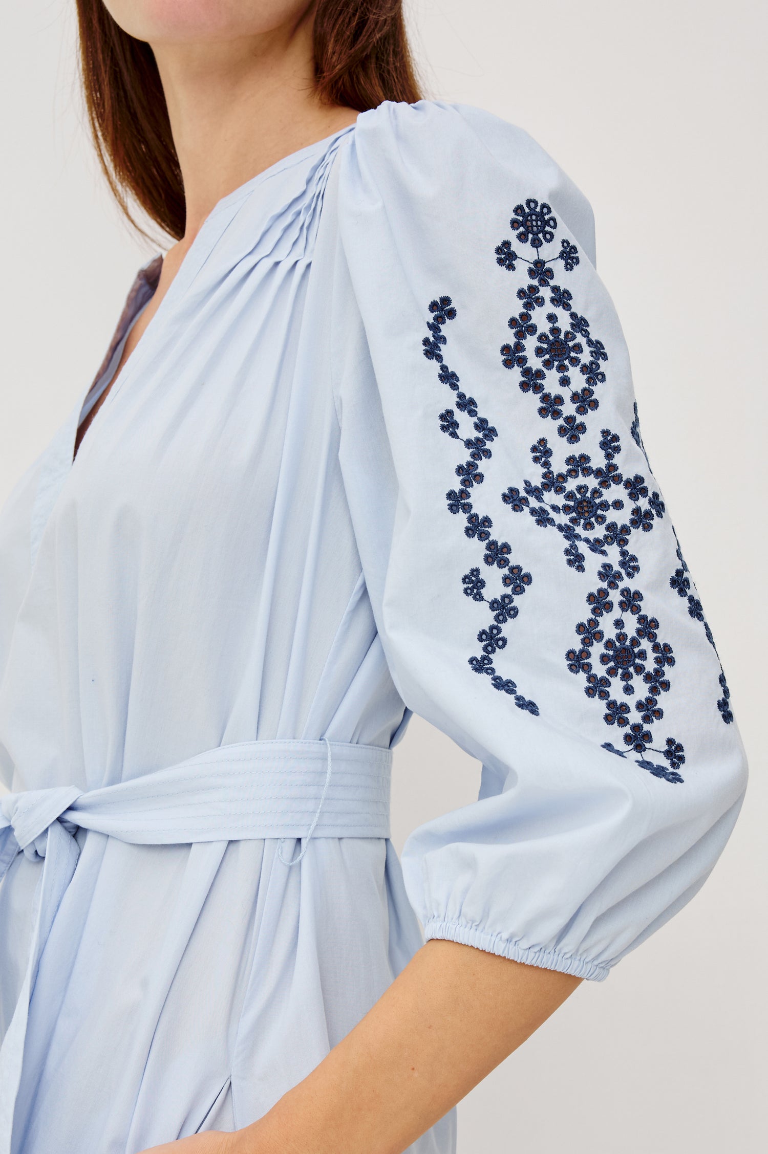 Carmel Peasant Maxi Dress in Poplin With Pleated Shoulders, V-Neckline, Three-Quarter Puff Sleeves, Adjustable Waist Ties, Side Pockets, Tiered Seam, and Contrast Embroidery at Cuffs and Hem in Blue Bird Colorway - Upper Body Close Up View Featured on Model