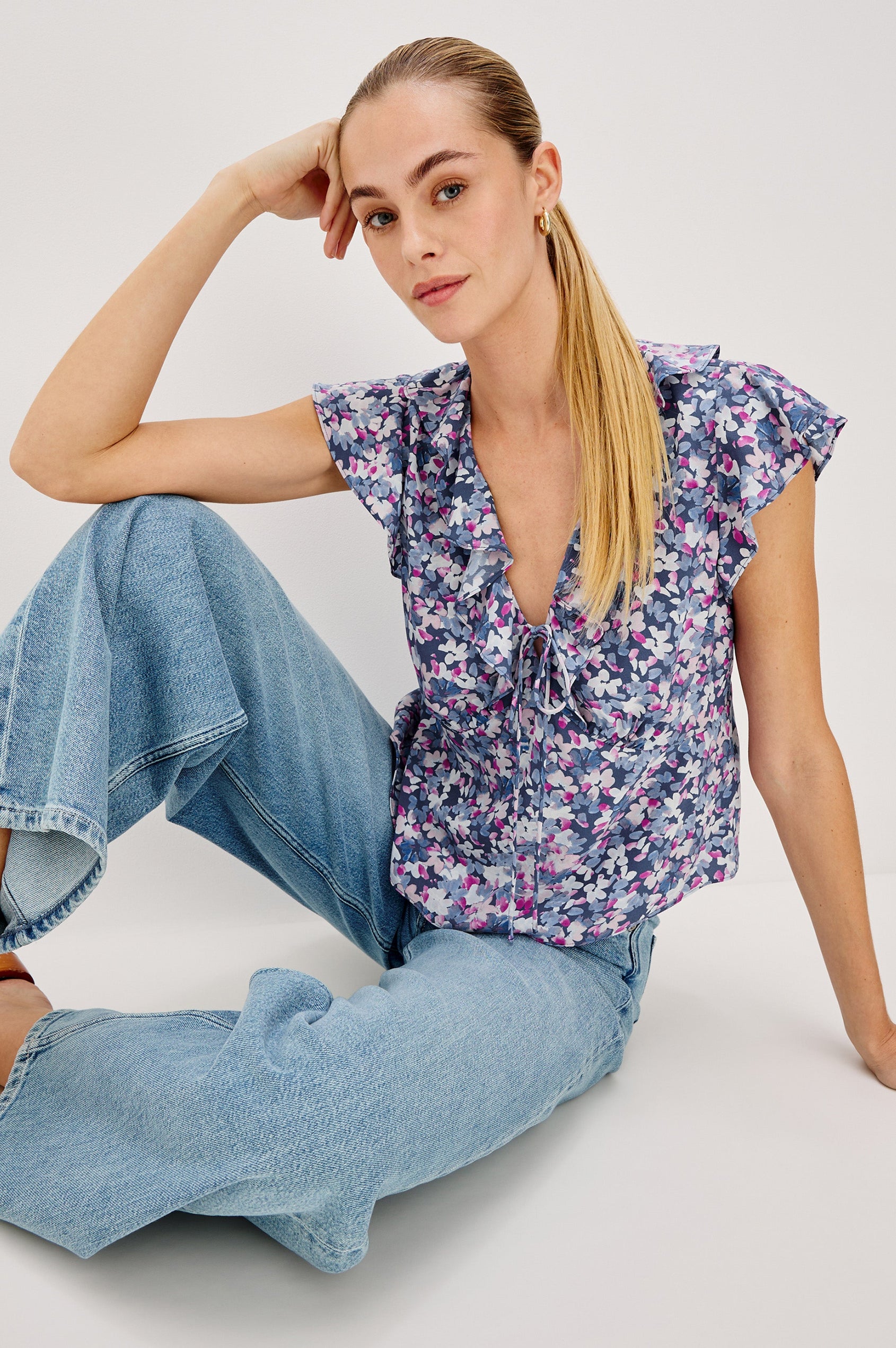 Carmine blouse, a chiffon top with ruffled cap sleeves, ruffles at the v-neckline, a front tie, and empire waist silhouette in Blue Blossom Colorway. Front View Shown on Model.