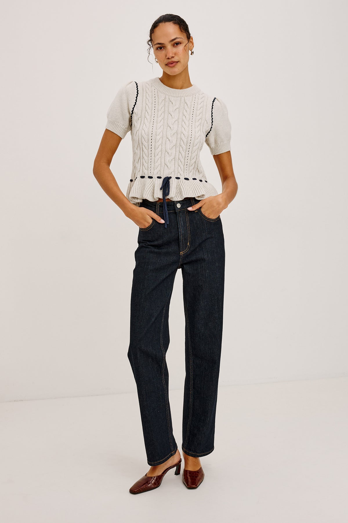 Chandi Sweater in Cable Knit With Short Puff Sleeves, Fitted SIlhouette, Soft Flared Peplum Hem, and Contrast Serpentine Trim and Interlocking Drawstring Ties in Heather Oat Colorway - Full Body Front View Featured on Model