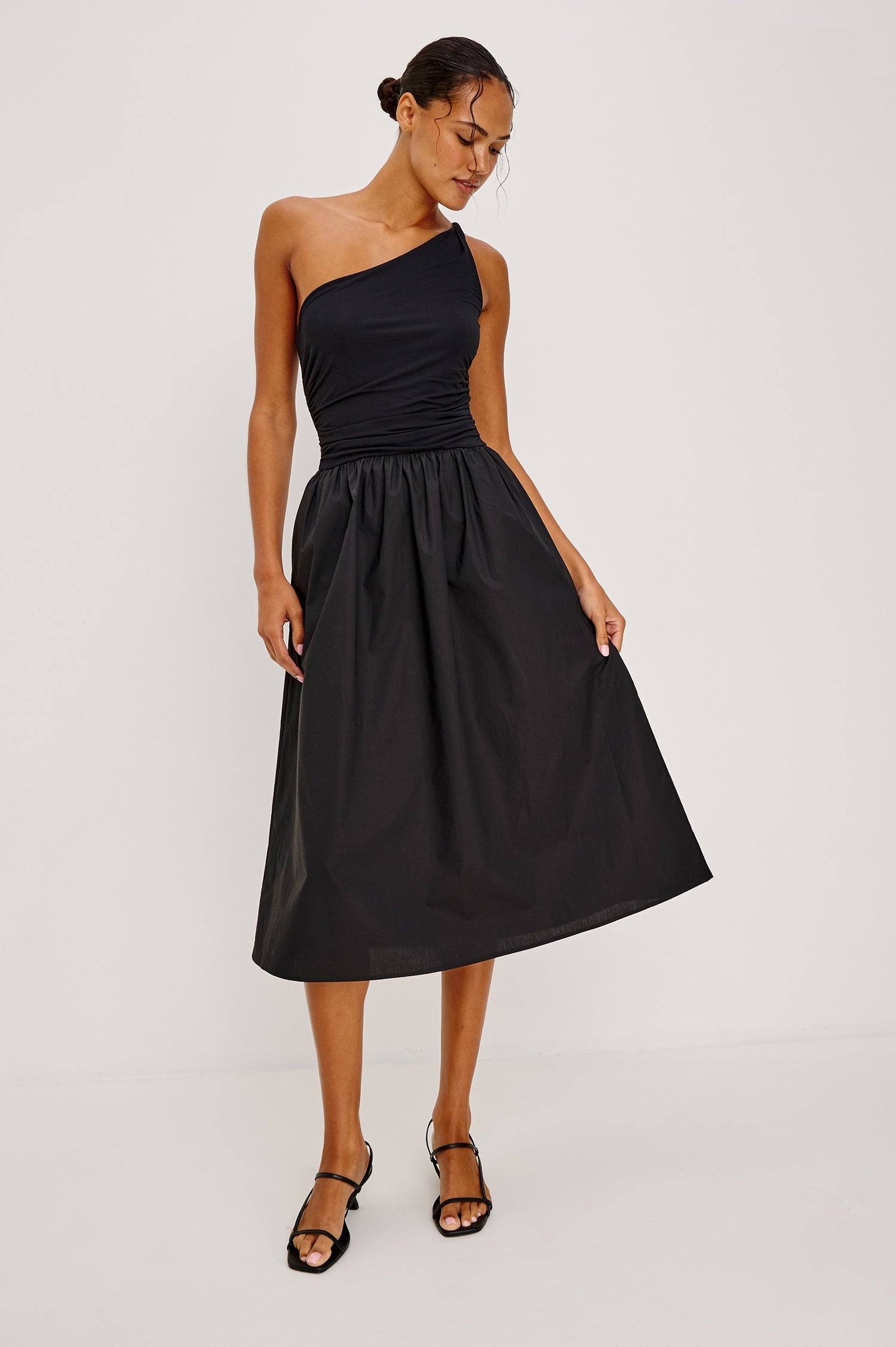 Chayana Midi Dress in Jersey With One-Shoulder Twist Strap Neckline, Waist Shirring, Side Pockets, Poplin Skirt in Black Colorway - Full Body Front View Featured on Model