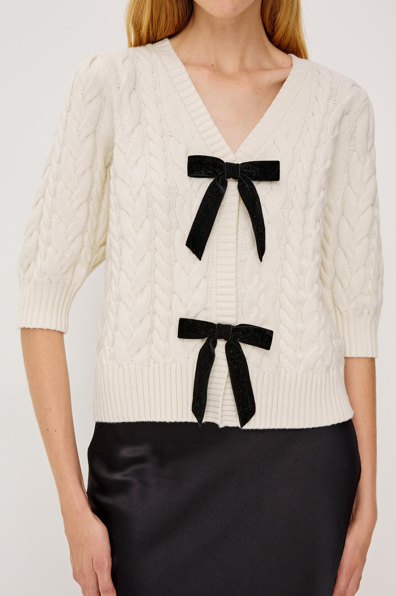 Clarissa Cardigan in Cable Knit and Relaxed Fit With V-Neckline, Contrast Velvet Bows With Front Hidden Snap Closures, and Three-Quarter Puff Sleeves - Mid Body Front View Featured on Model Sitting