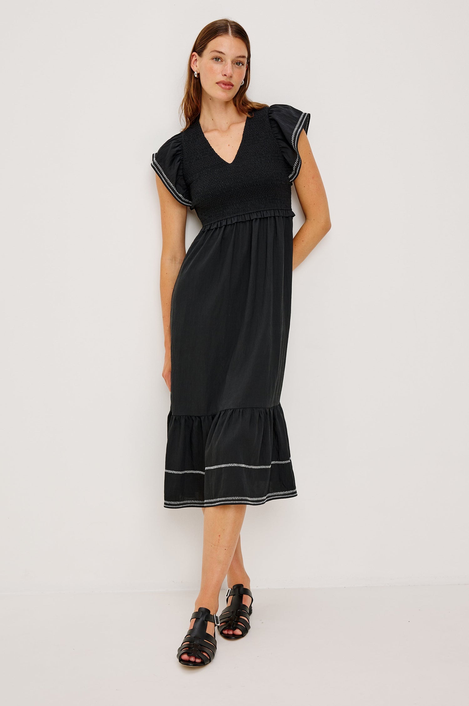 Clementine Midi Dress with a Deep V Neckline, Flutter Sleeves, Smocked Top, Two Side Pockets and contrast white stitching on the Sleeves and Hem in Black Colorway- Front Full Body View Featured on Model.