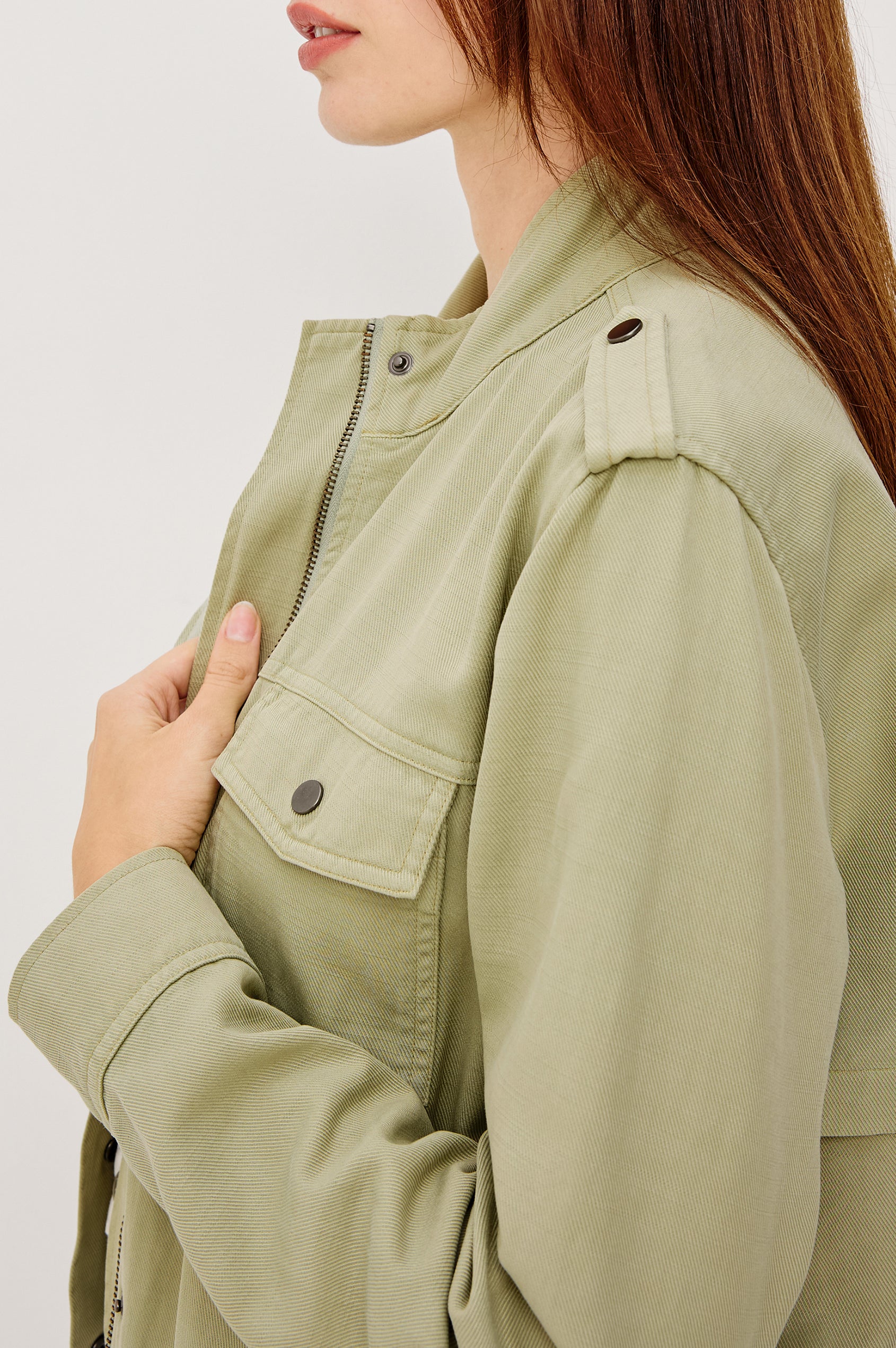 Collins Miitary Inspired Jacket With Shoulder Epaluettes Stand Collar Front Snap Buttons Double Chest Pockets Long Sleeves in Vintage Sage Colorway - Side Upper Body Close Up View Featured on Model