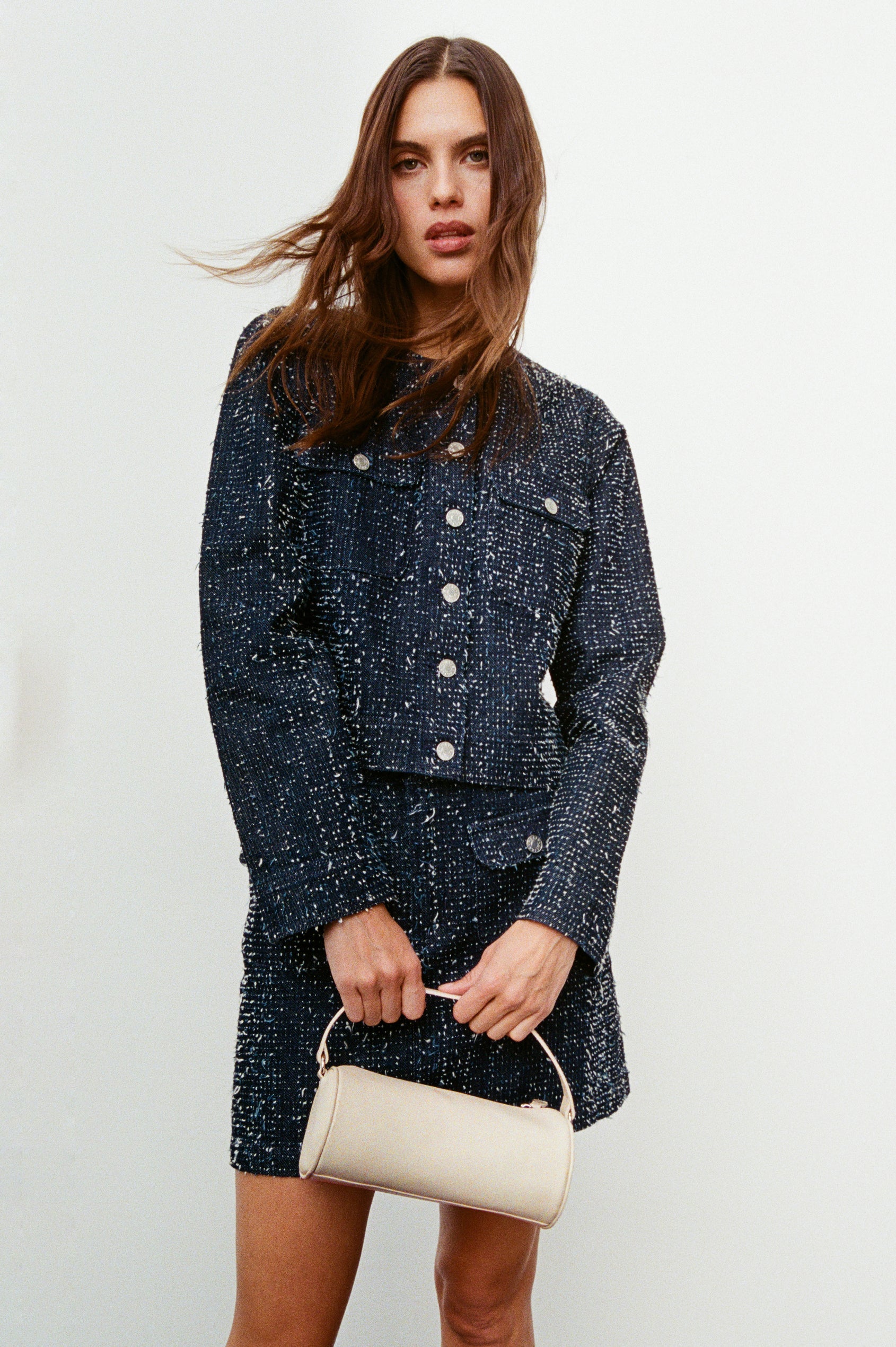 The Como is a mini barrel bag, made from smooth leather with a fixed top strap, a removable and adjustable buckled crossbody strap, a top zip, a side-embossed logo, and a branded interior label, in Bone Leather colorway. Front full body view featured on model.