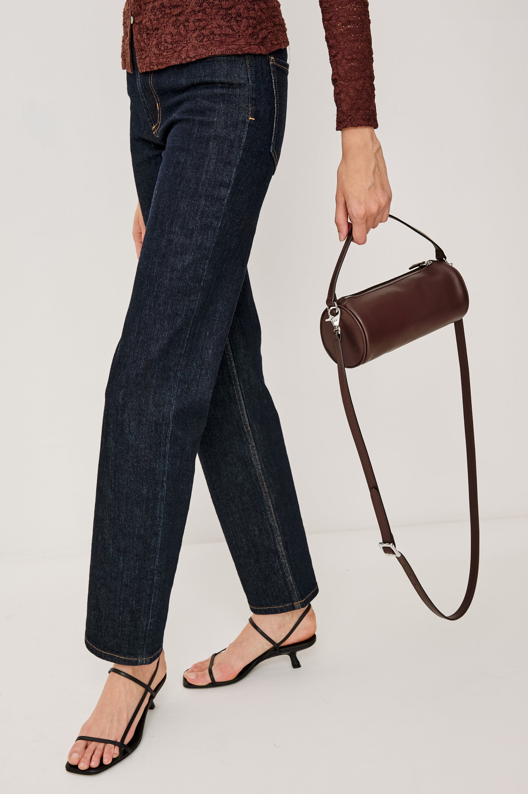 The Como is a mini barrel bag, made from smooth leather with a fixed top strap, a removable and adjustable buckled crossbody strap, a top zip, a side-embossed logo, and a branded interior label, in Espresso colorway. Back full body view featured on model.