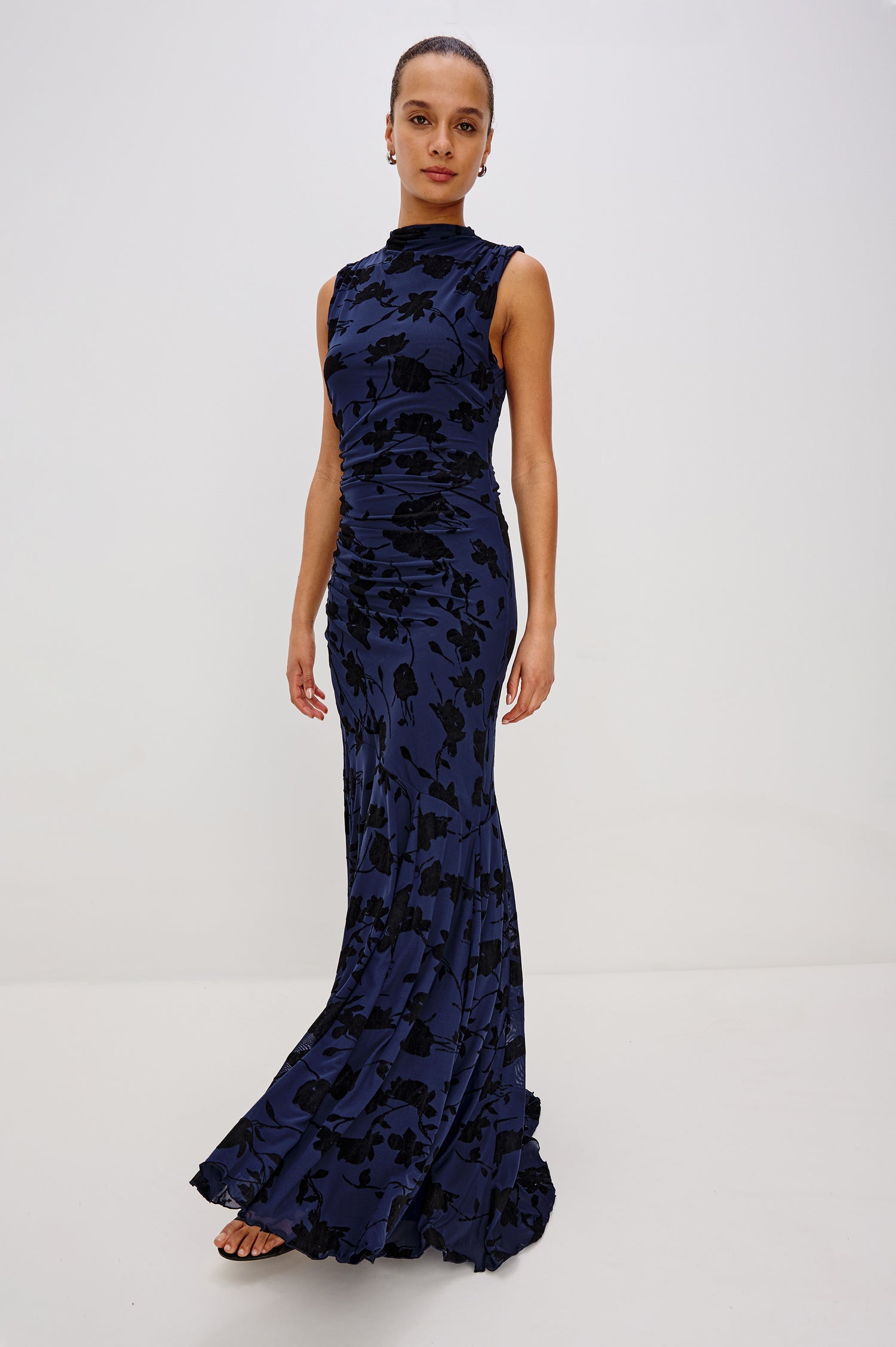Cosmos Maxi-Length Dress with a Cowl Neck, Sleeveless, Form Fitting with a Ruched Side Seam Detail and an A-line Hem in Navy Tossed Roses Colorway. Full Body Front View Shown on Model.