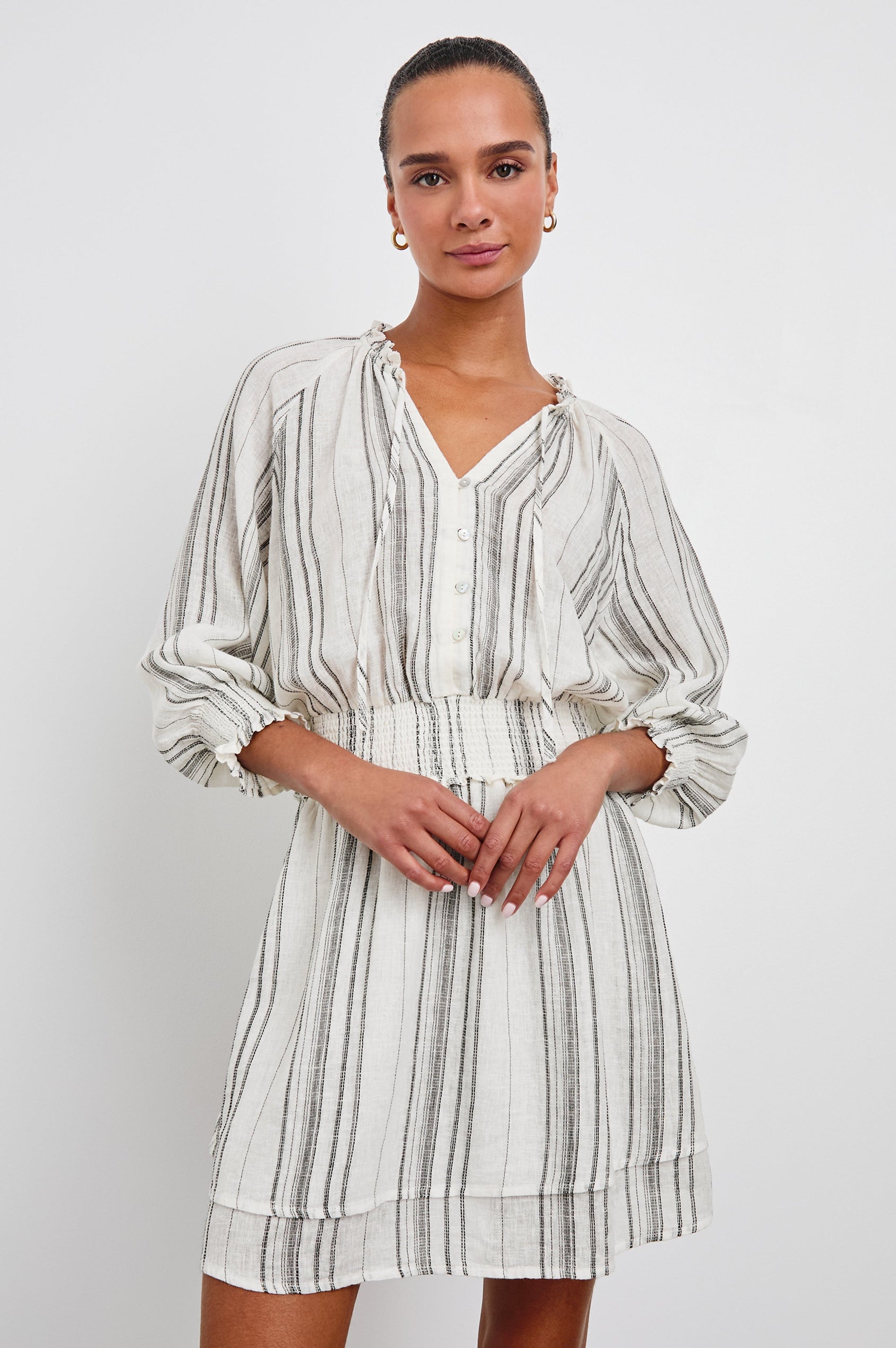 Crystal Mini Dress with Mid-Length Sleeves, Shirred Cuffs and Waist, a V Neck, Ties at the Collar, and Buttons down the Bodice in Basque Stripe Colorway, Thin Black Vertical Stripes on White - Front View Featured on Model 
