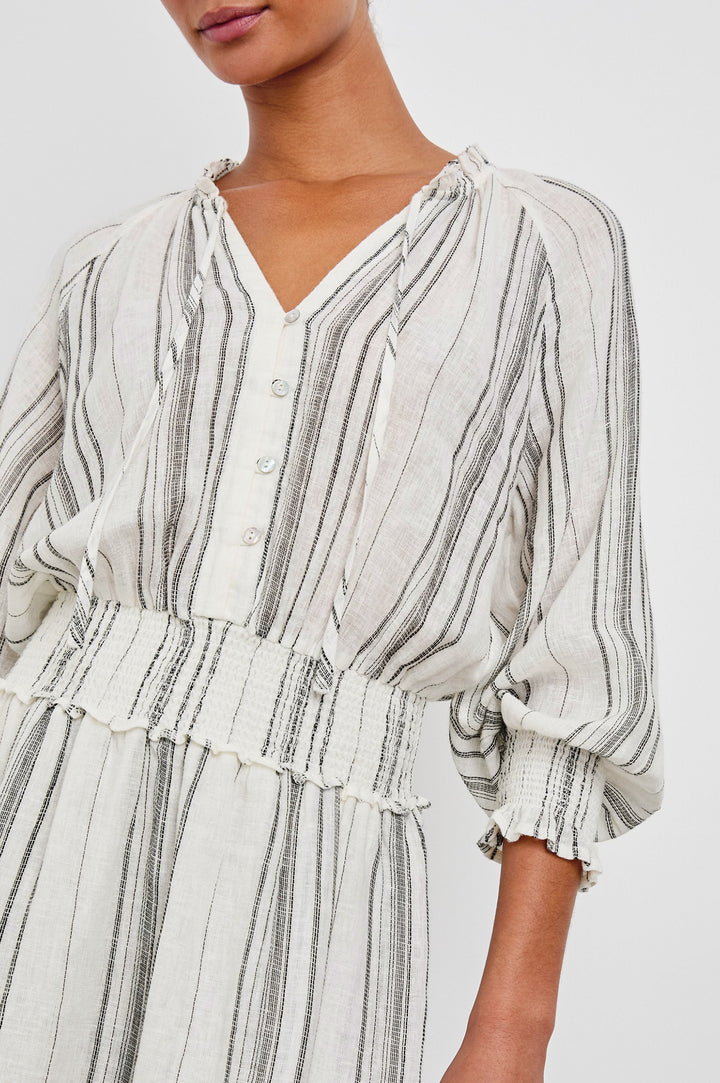 Crystal Mini Dress with Mid-Length Sleeves, Shirred Cuffs and Waist, a V Neck, Ties at the Collar, and Buttons down the Bodice in Basque Stripe Colorway, Thin Black Vertical Stripes on White - Front View Featured on Model 