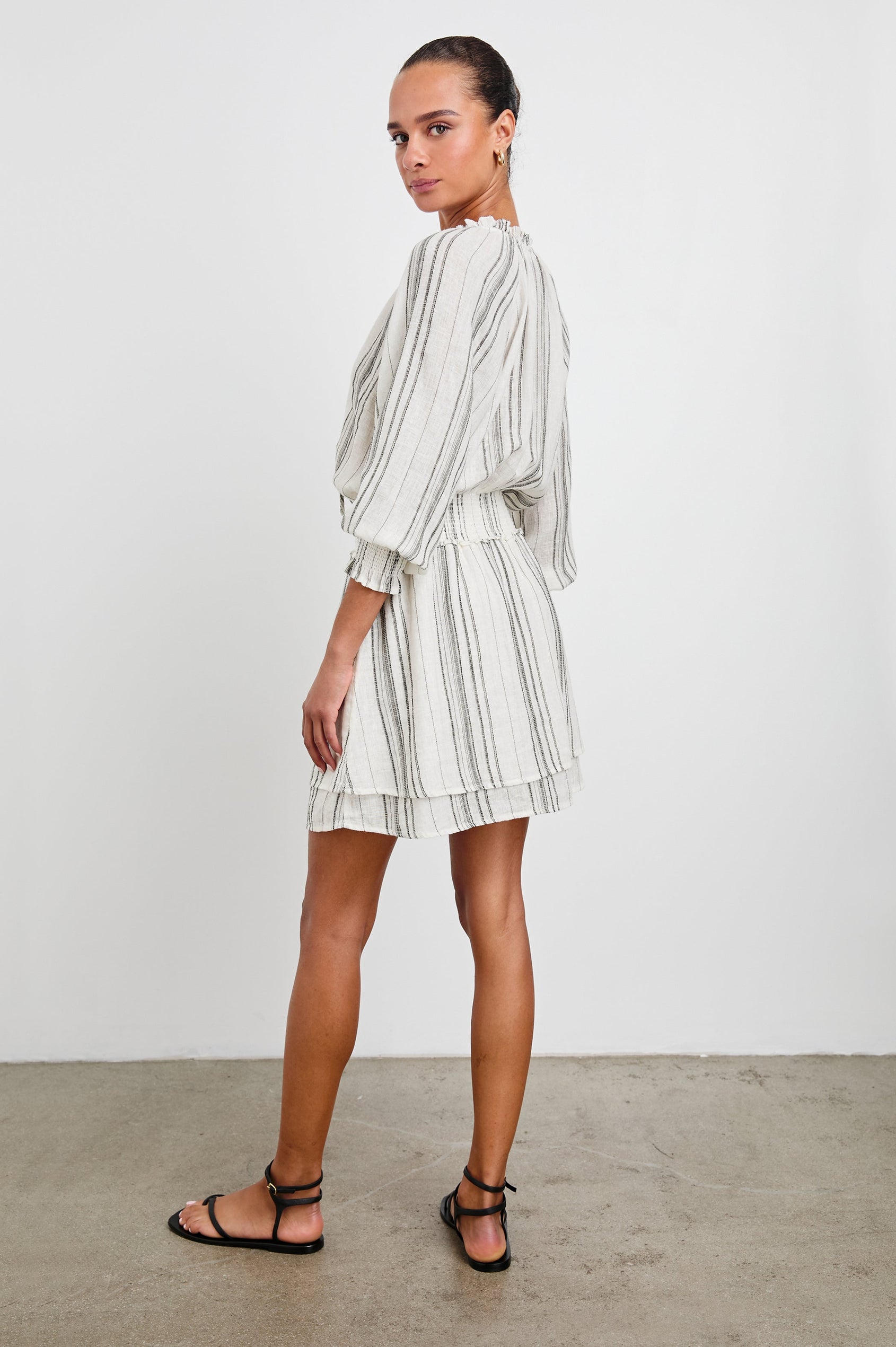 Crystal Mini Dress with Mid-Length Sleeves, Shirred Cuffs and Waist, a V Neck, Ties at the Collar, and Buttons down the Bodice in Basque Stripe Colorway, Thin Black Vertical Stripes on White - Side View Featured on Model 