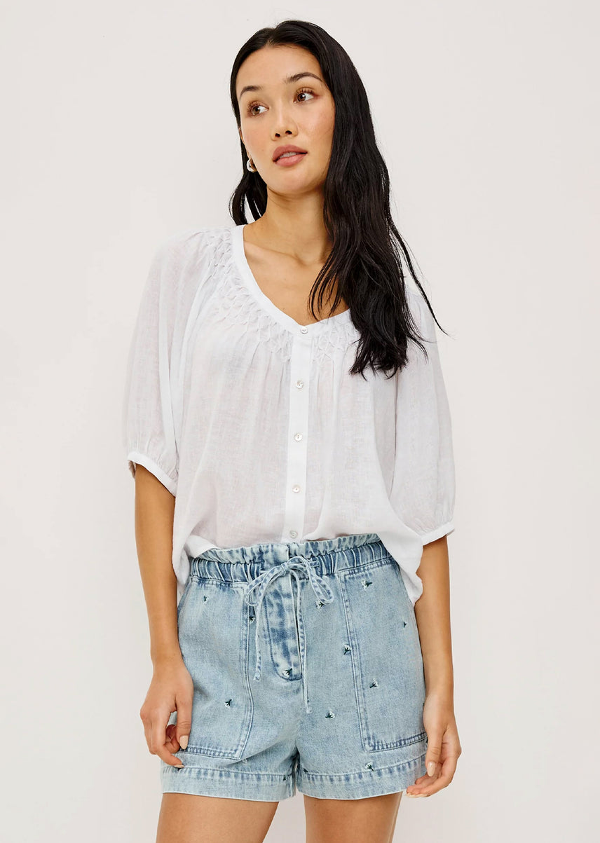 Woman wearing a white blouse and denim shorts on a plain background