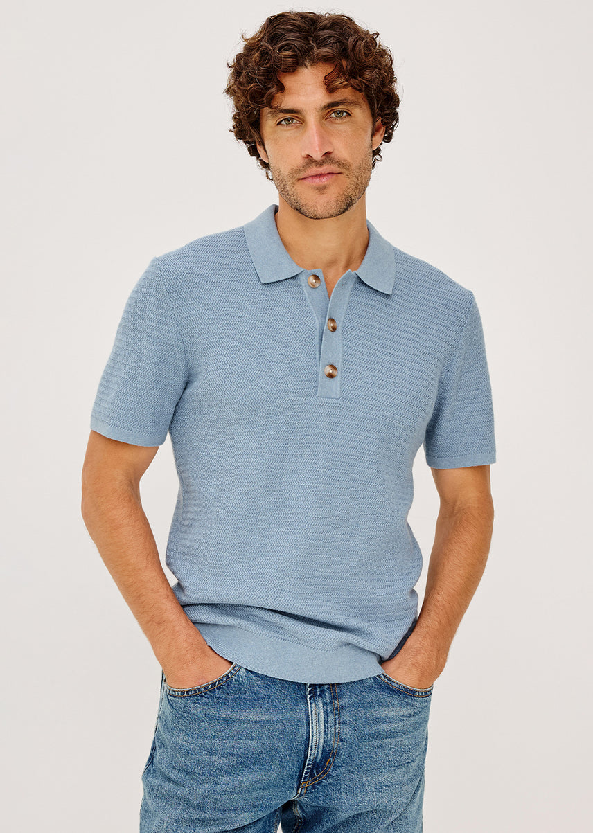 Man wearing a blue striped polo shirt and jeans on a light gray background