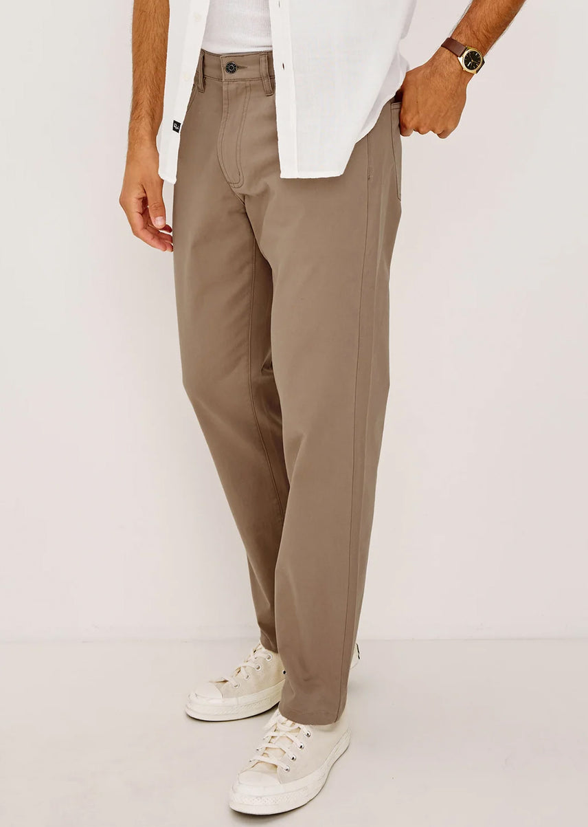 Person wearing beige pants with a white shirt and white sneakers on a plain background